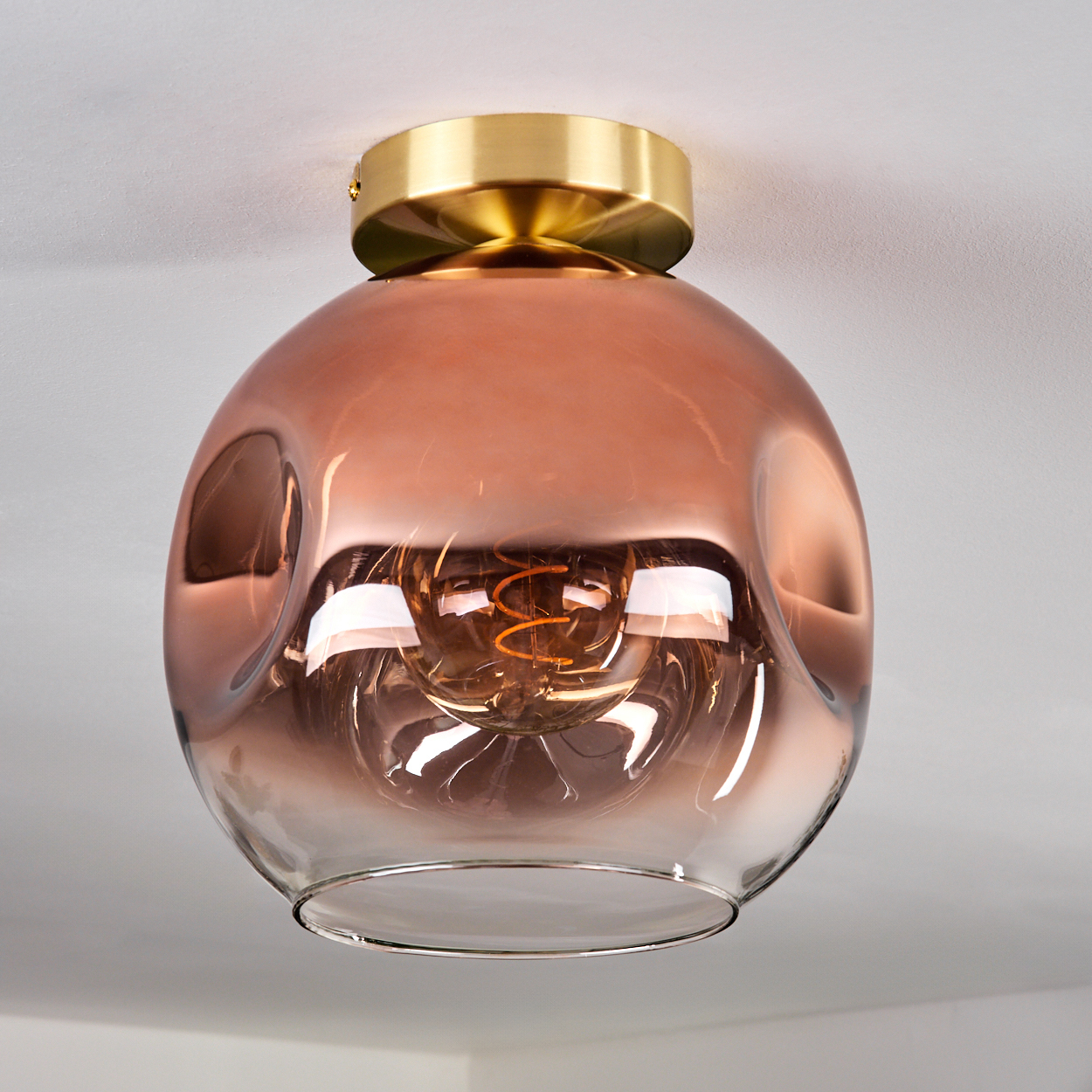 Eine moderne Deckenleuchte mit bronzefarbenem Glasschirm und Messingfuß. Die Glühbirne ist durch das Glas sichtbar.