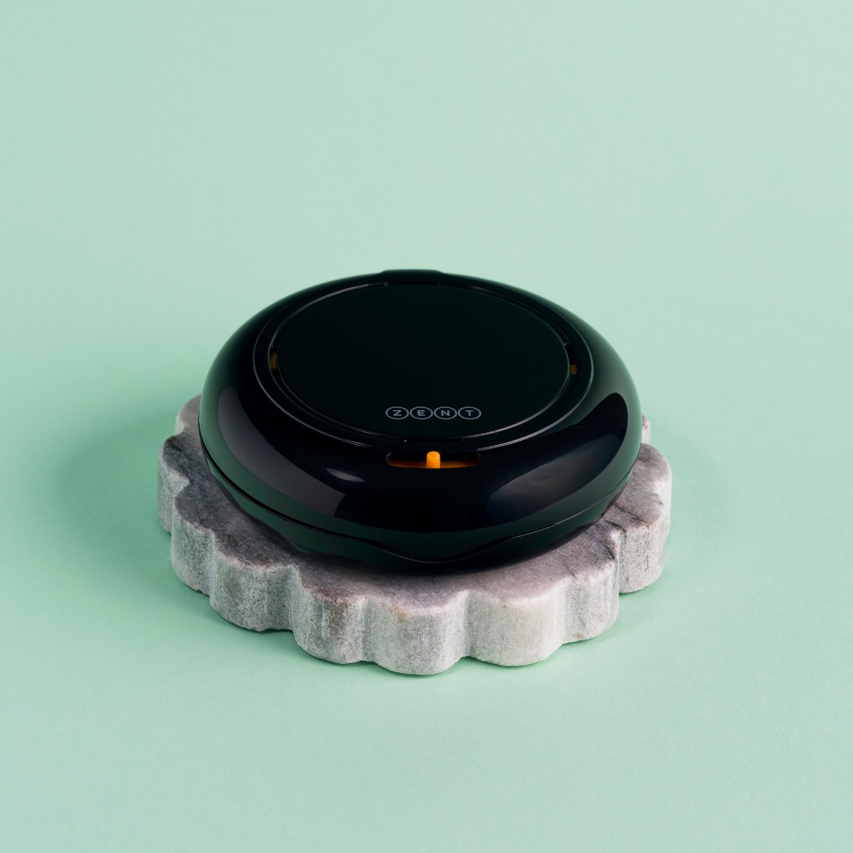 Czarne, okrągłe urządzenie z napisem 'ZENT' stoi na szarej, muszlowej kamiennej podstawie na jasnym zielonym tle.