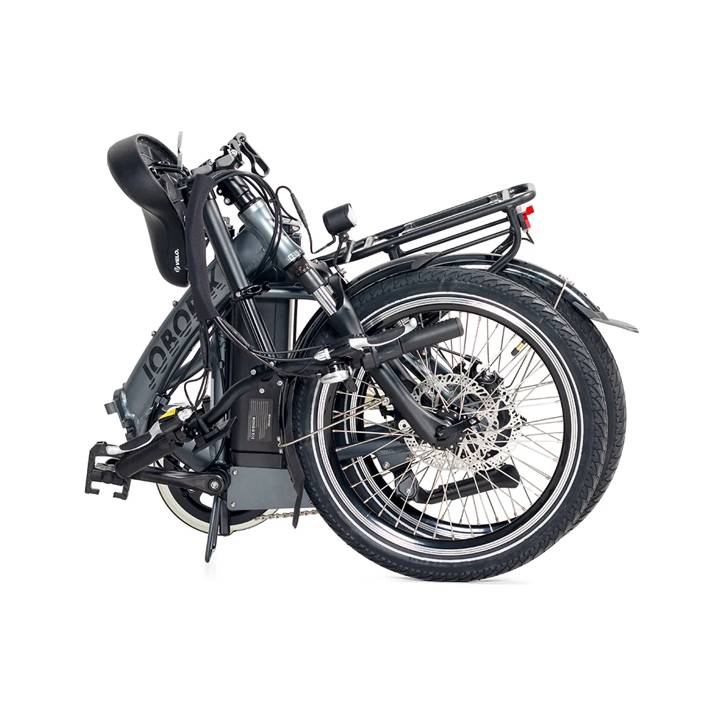 Złożony szary rower elektryczny na białym tle. Rower ma czarne opony, bagażnik i akumulator. Kierownica jest złożona.