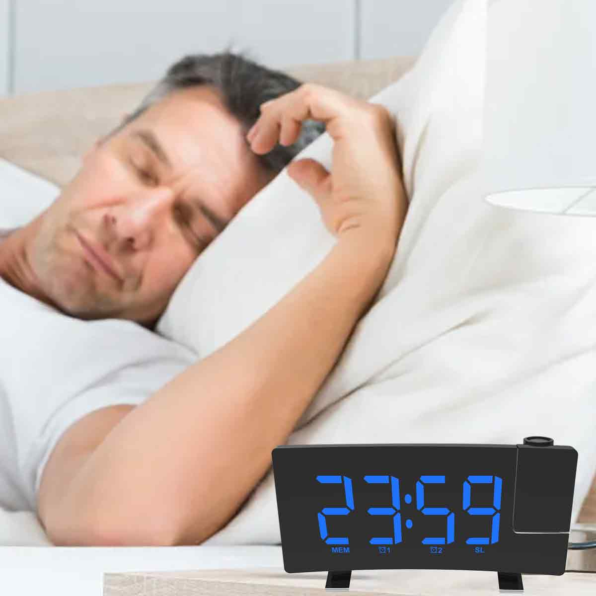 Ein Mann schläft im Bett. Eine Digitaluhr zeigt 23:59. Der Arm des Mannes liegt auf einem Kissen.