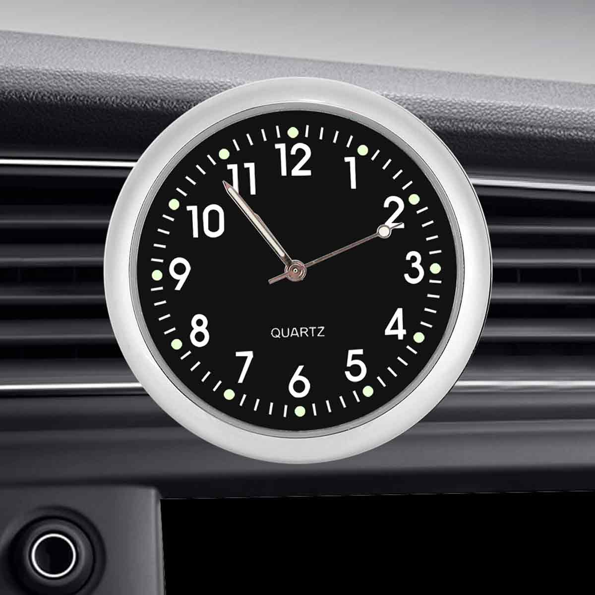 Eine Auto-Uhr mit schwarzem Zifferblatt und weißen Zahlen. Die Uhr befindet sich in einem silbernen Rahmen und ist auf dem Armaturenbrett befestigt.