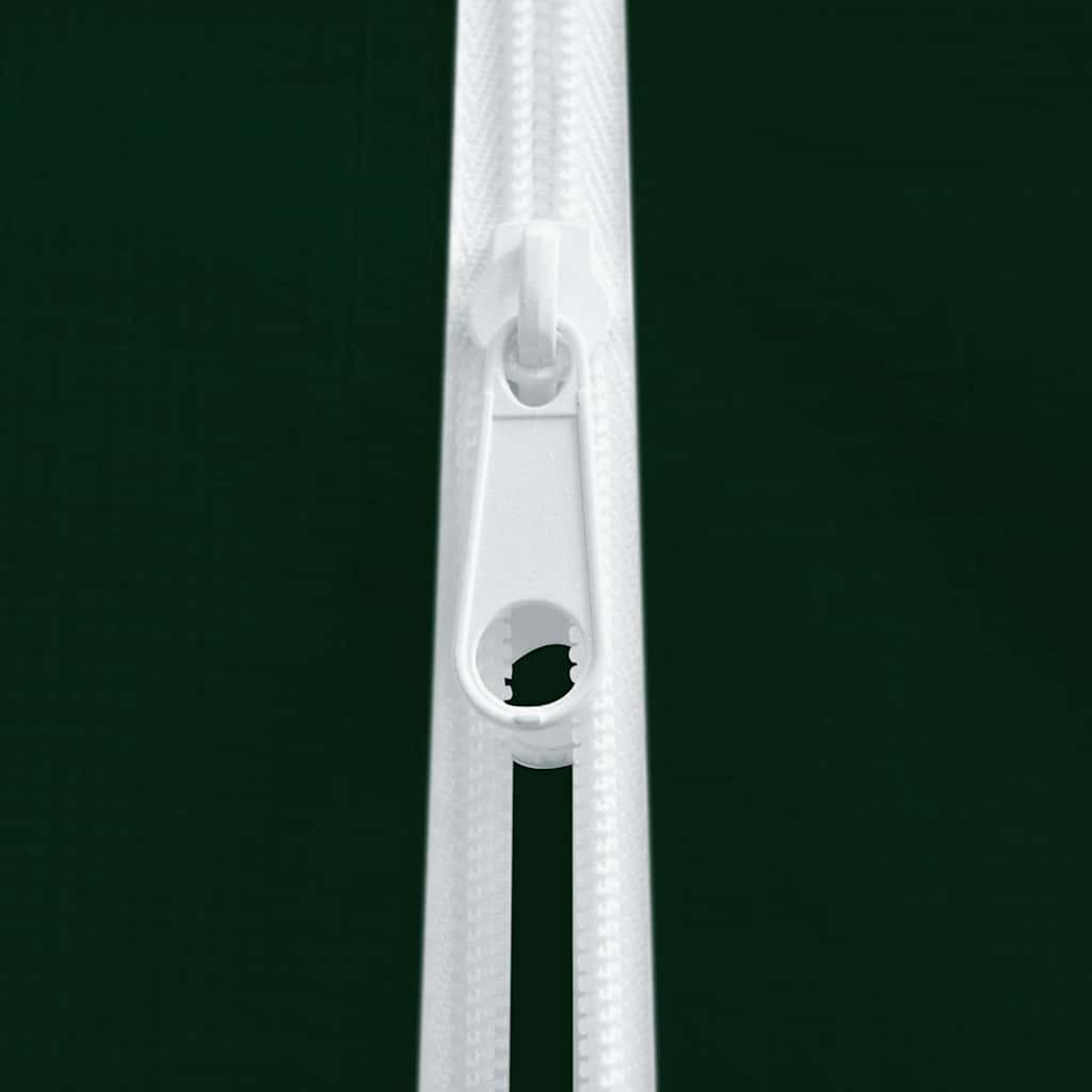 Primer plano de una cremallera blanca sobre un fondo verde oscuro. La cremallera está centrada, con la pestaña visible. El fondo es liso.