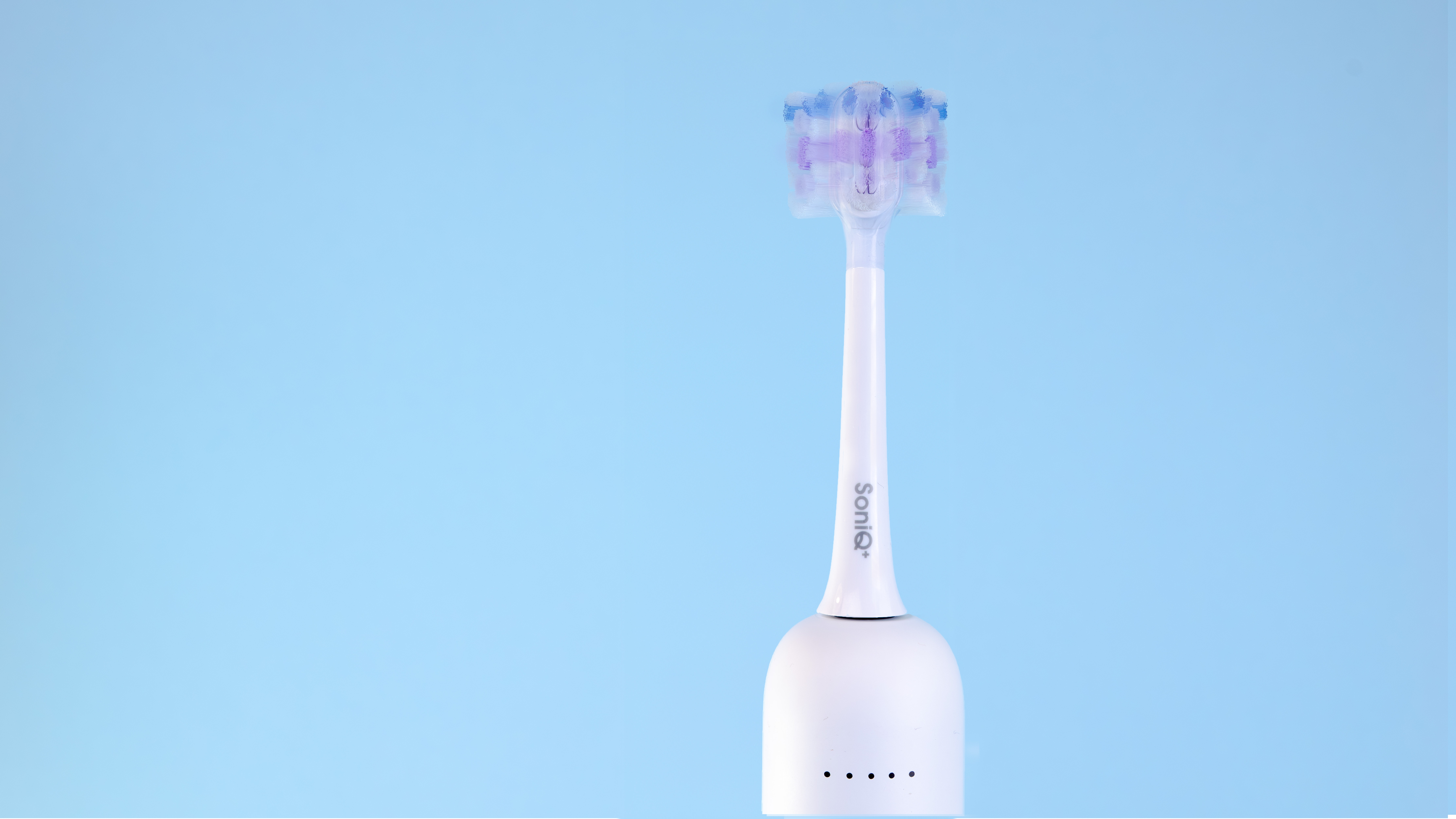 Elektryczna szczoteczka do zębów na niebieskim tle. Szczoteczka jest biała z fioletowym i niebieskim włosiem. Podstawa ma kontrolki.