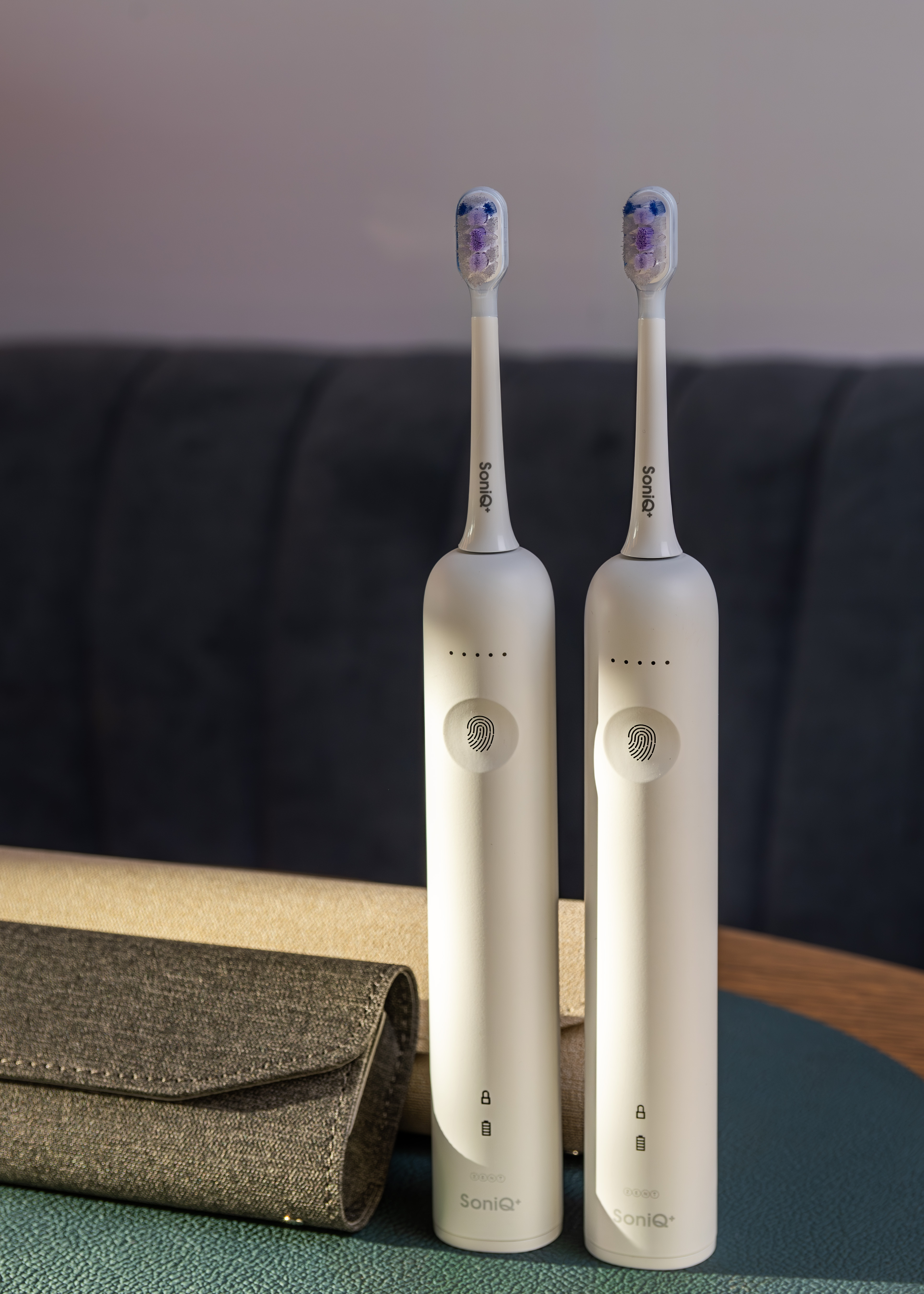 Dwie białe elektryczne szczoteczki do zębów. Szare etui i tło. Szczoteczki na zielonej powierzchni.