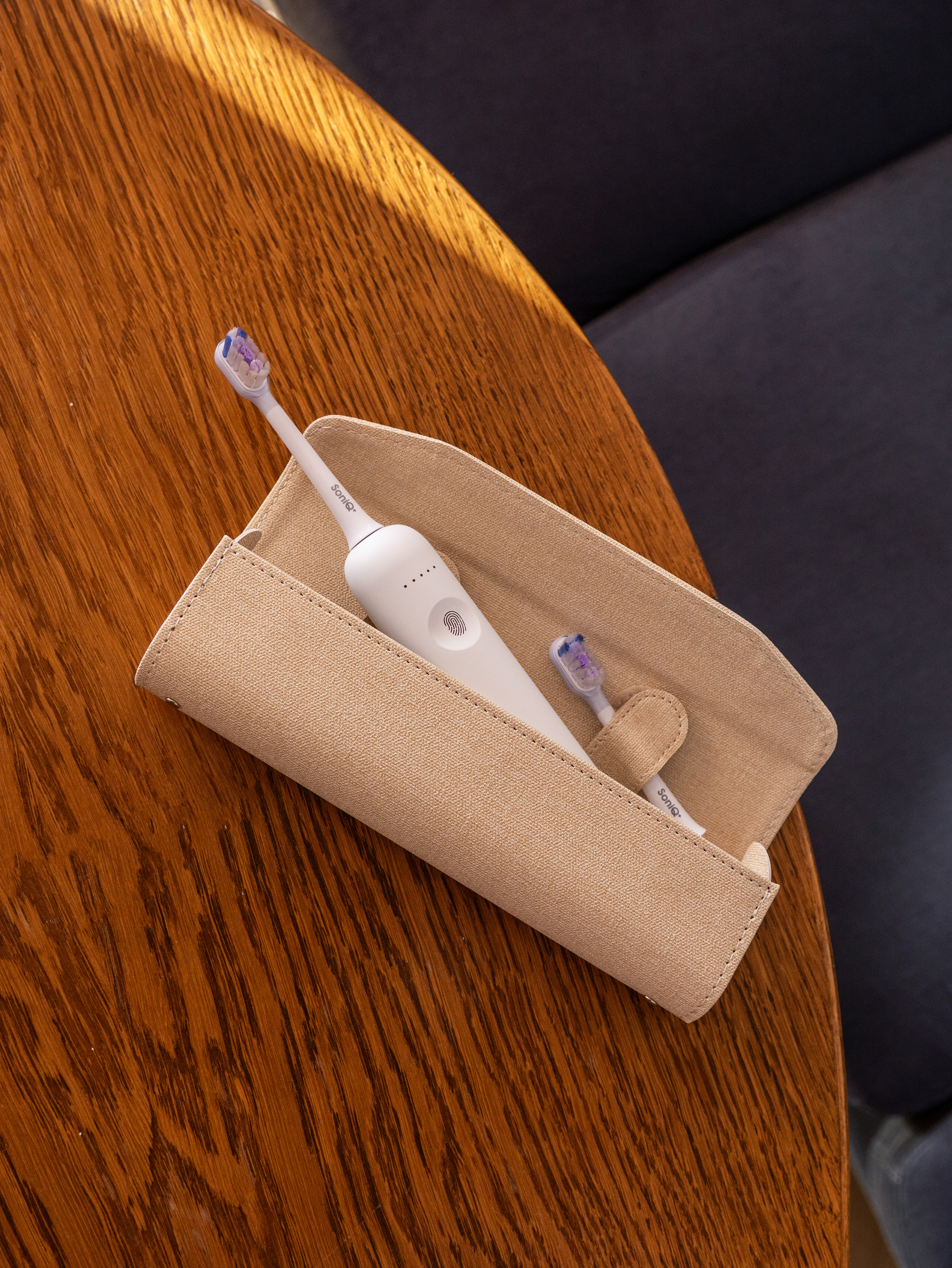 Biała elektryczna szczoteczka do zębów i zapasowa główka w beżowym etui na drewnianym stole.