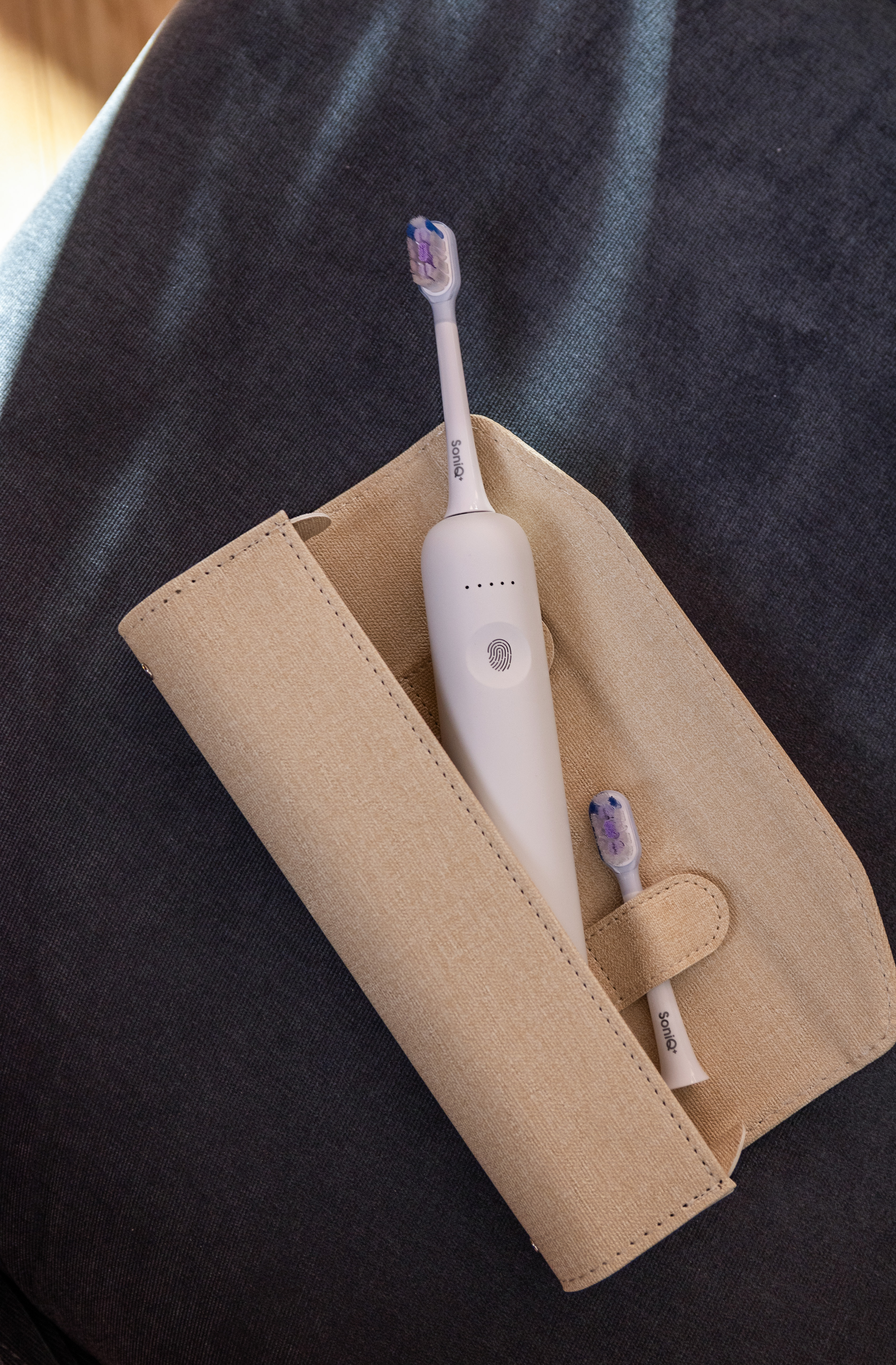 Biała szczoteczka elektryczna w beżowym etui na ciemnoszarej powierzchni. Dodatkowa końcówka szczoteczki w etui.