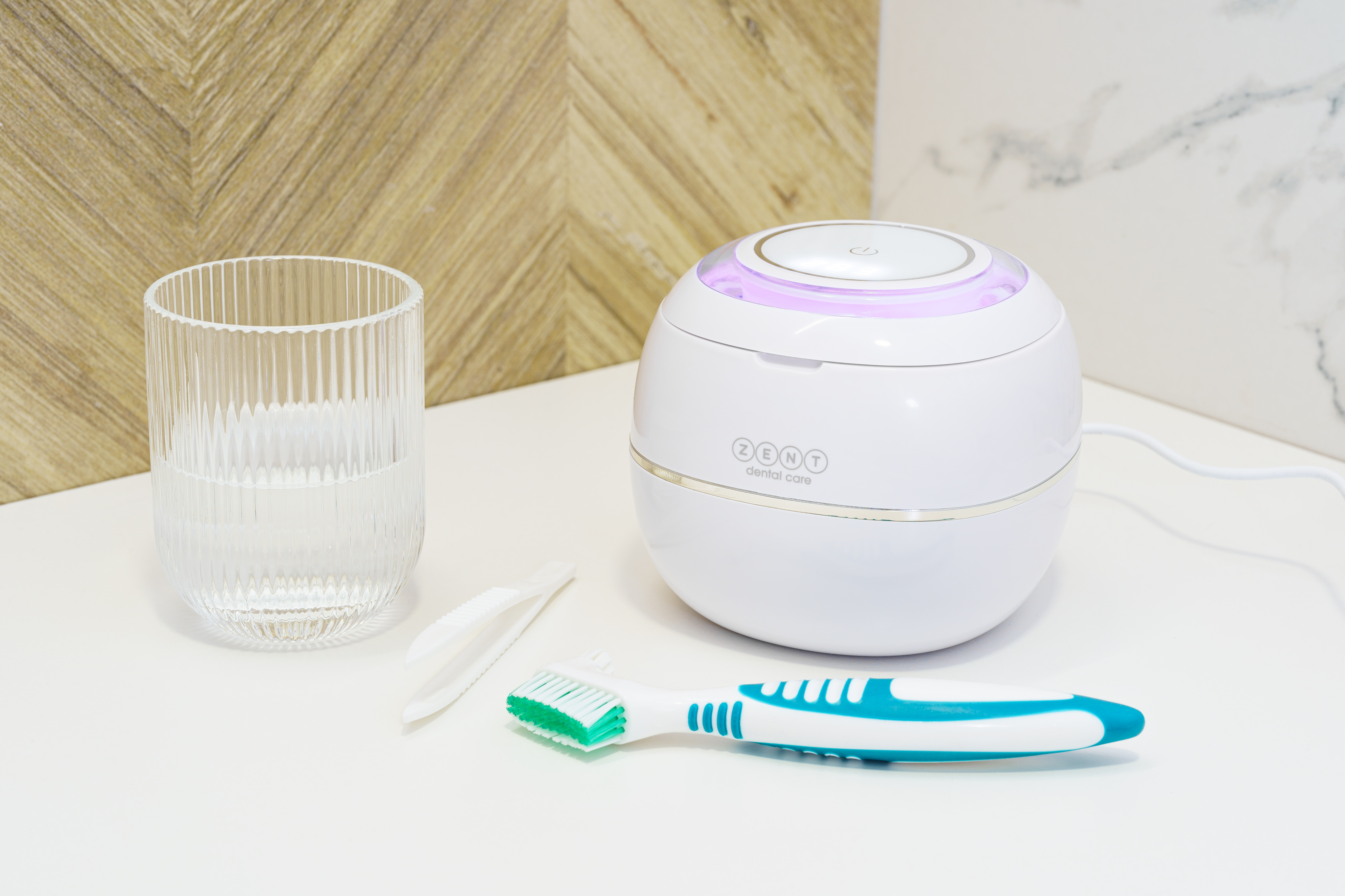 Białe urządzenie do pielęgnacji zębów, szczoteczka do zębów, szklanka z wodą na białej powierzchni. Drewniane i marmurowe tło.