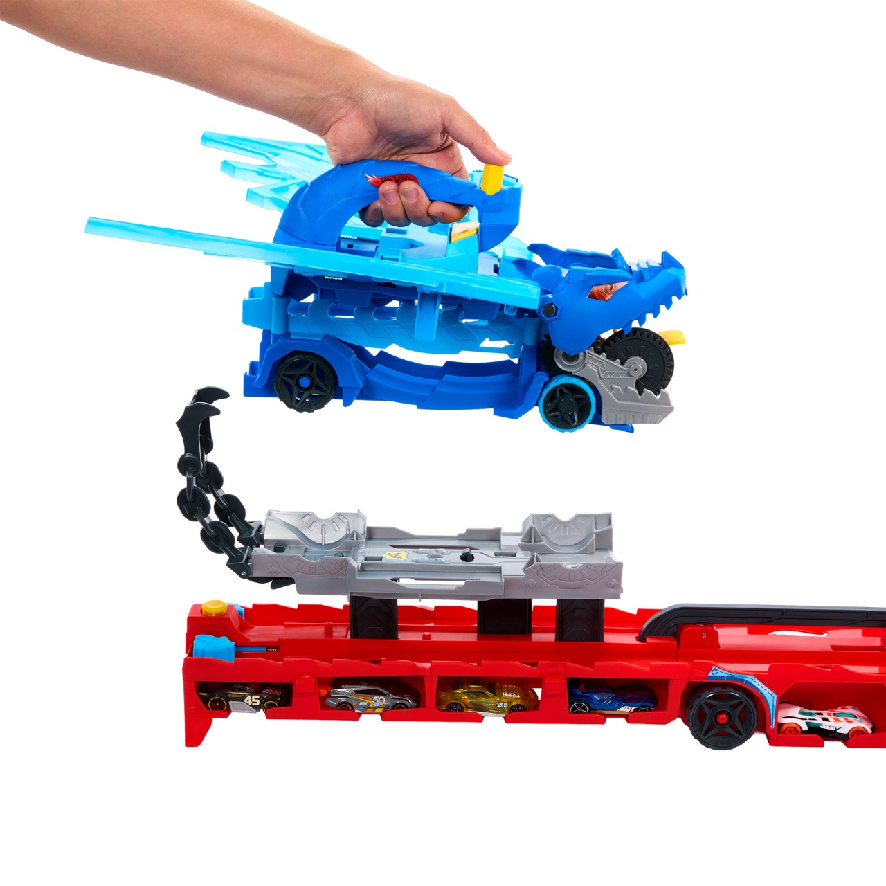 Una mano sostiene un juguete azul con forma de dragón sobre un camión de juguete rojo con coches pequeños dentro. Una cadena negra conecta los juguetes.