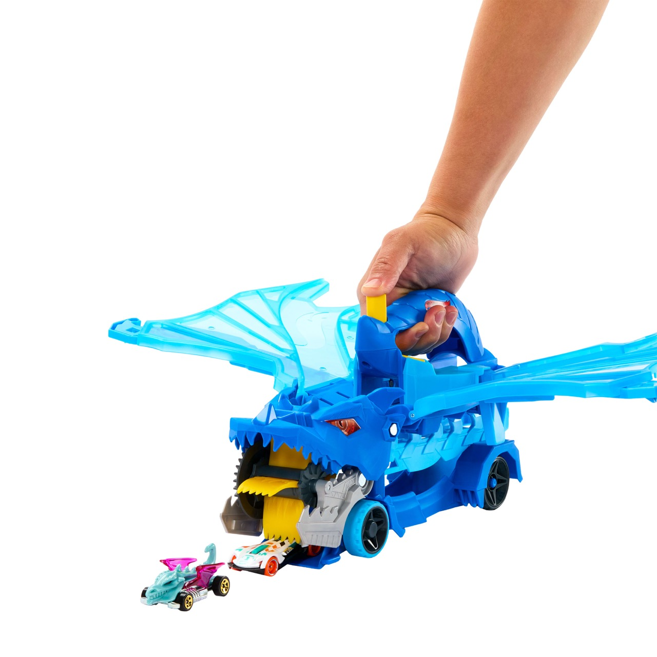 Una mano sostiene un juguete de dragón azul con coches dentro. El dragón tiene alas y una boca que se abre. Los coches son coloridos.