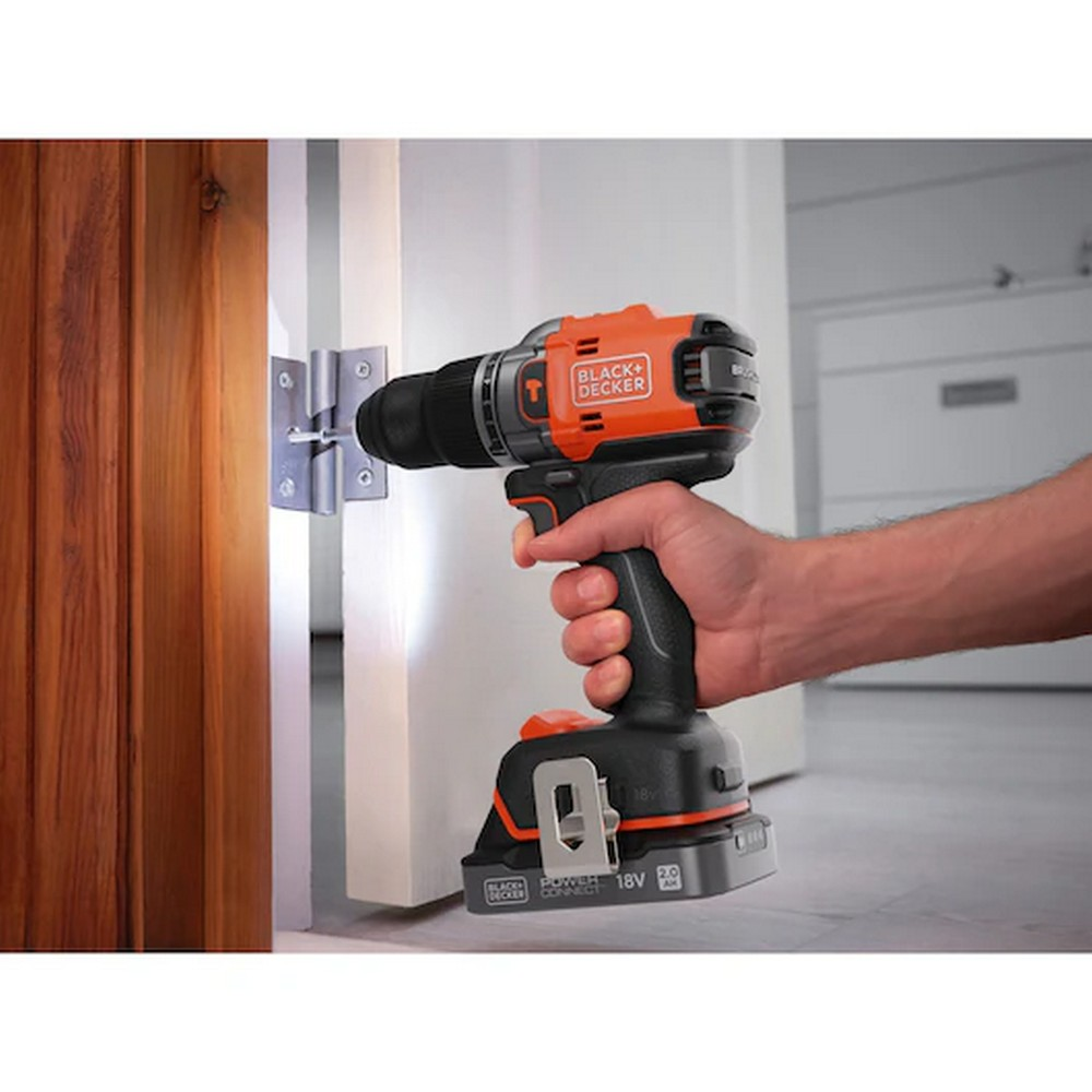 Bir kişi, beyaz bir kapıya menteşe takmak için turuncu ve siyah bir Black+Decker matkap kullanıyor. Solda ahşap bir kapı var.