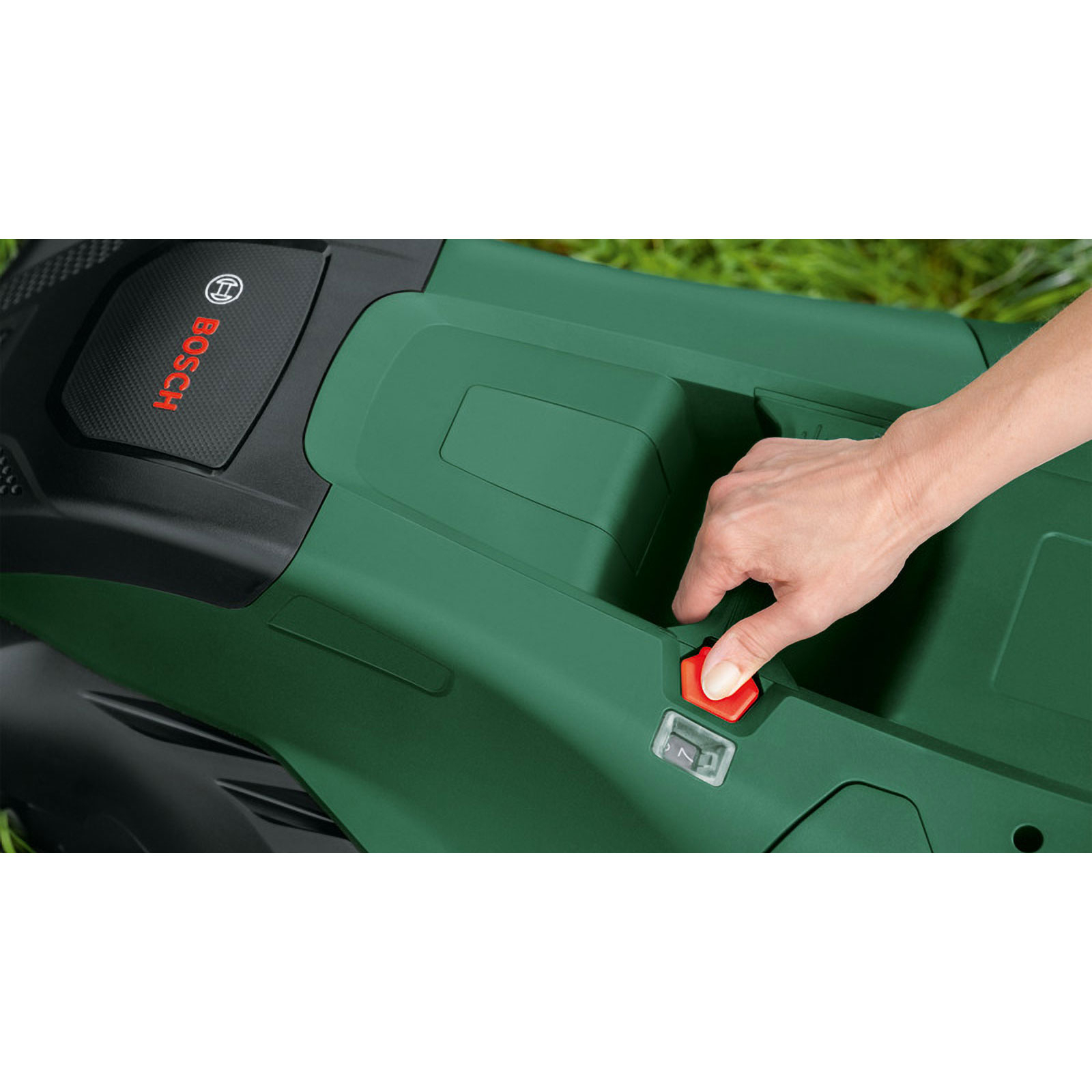 Eine Hand drückt einen roten Knopf auf einem grünen Rasenmäher. Das Bosch-Logo ist sichtbar. Grünes Gras ist der Hintergrund.