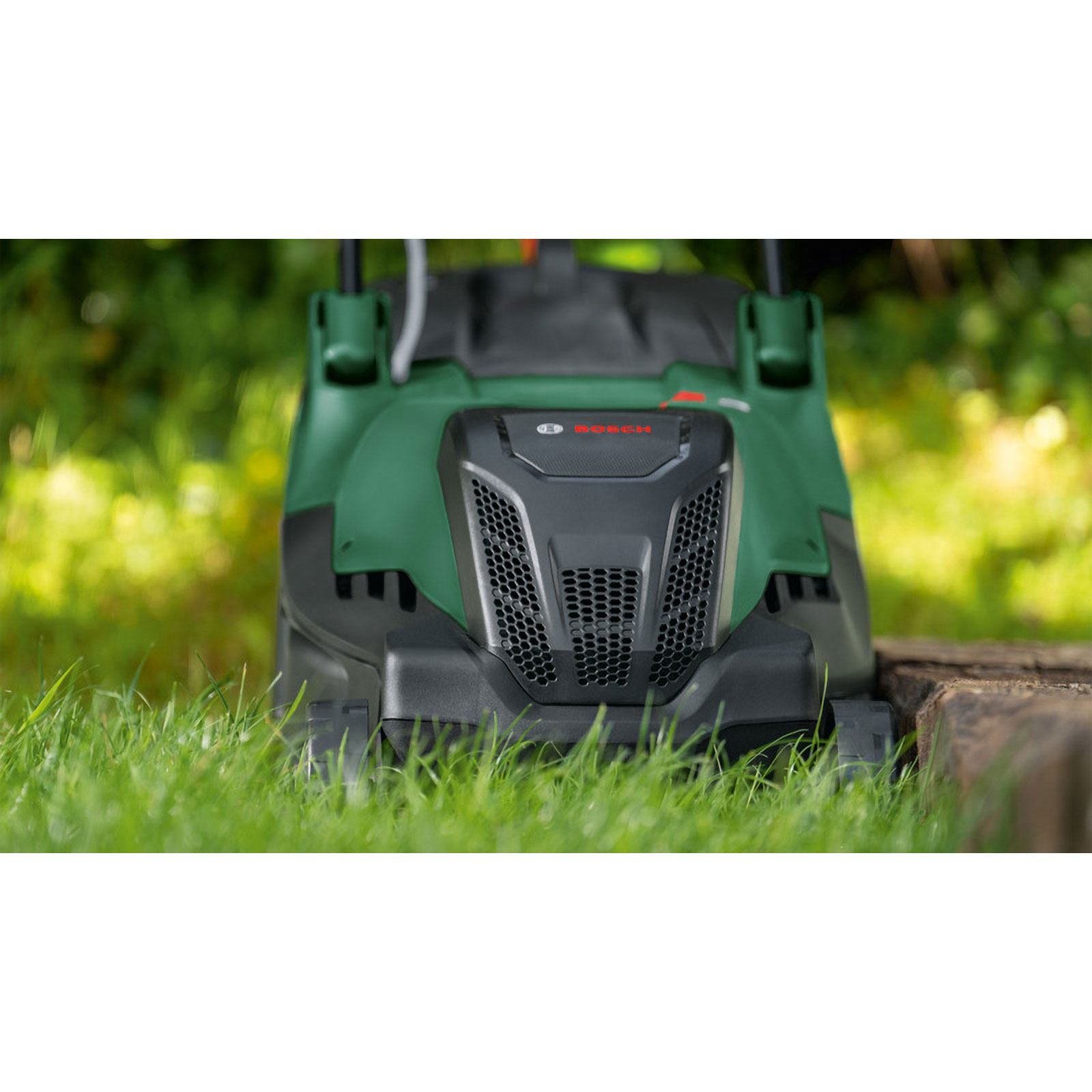 Grüner Bosch-Rasenmäher im Gras. Schwarze Front mit Wabenmuster. Bosch-Logo. Holzumrandung im Hintergrund.
