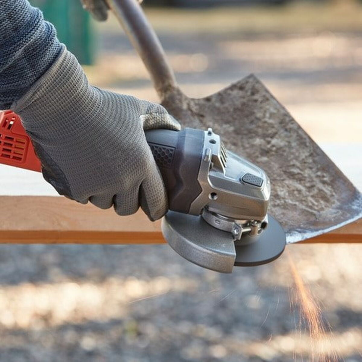 Ręka w rękawicy używa szlifierki na drewnie. Iskry lecą. Łopata jest w tle.