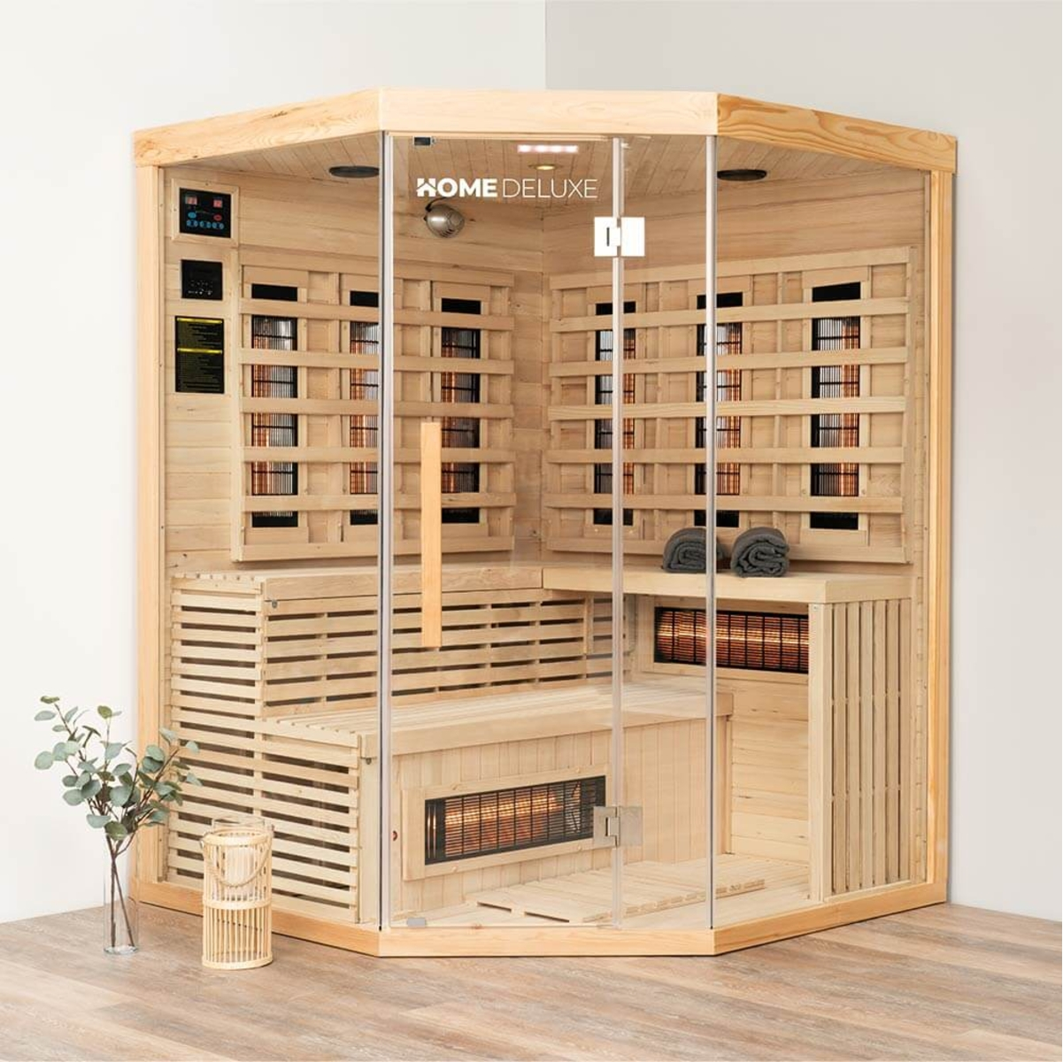 Eine holzgefertigte Heimsauna mit Glastüren. Innen befinden sich Bänke und Heizelemente. Davor stehen eine Pflanze und eine dekorative Laterne.