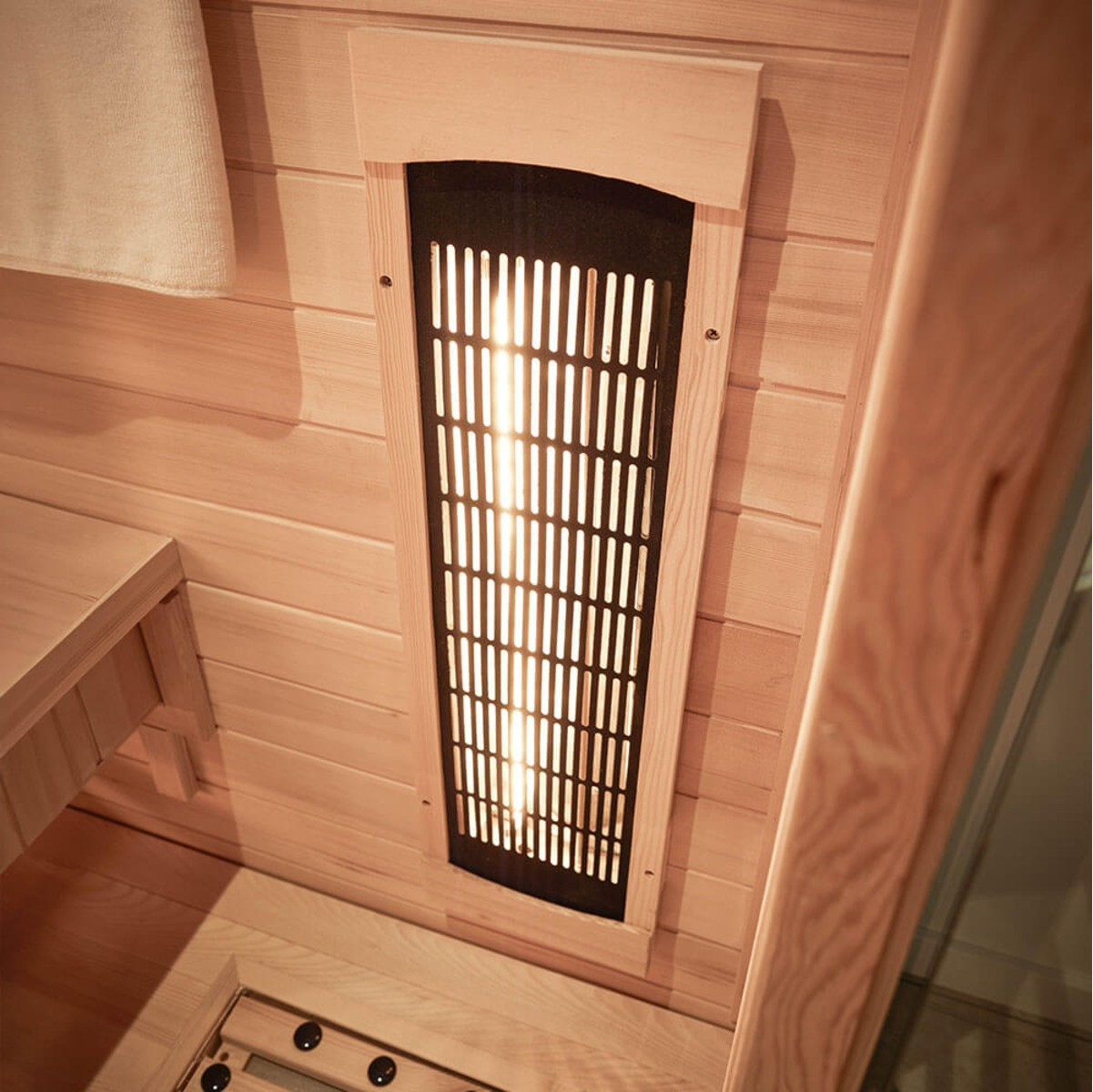 In einer Sauna mit Holzwänden. Ein glühendes Heizelement ist sichtbar. Auf der linken Seite hängt ein Handtuch. Bank- und Bodendetails sind zu sehen.
