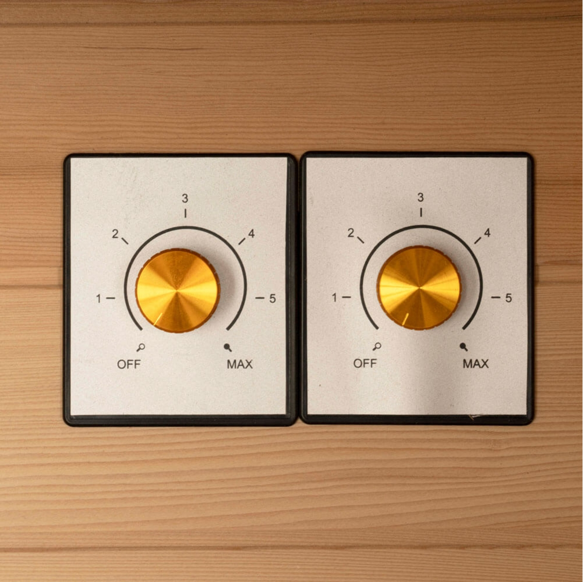 Zwei Bedienfelder mit goldenen Knöpfen und den Zahlen 1-5. Unter den Knöpfen befinden sich die Aufschriften 'OFF' und 'MAX', vor einem Holzgrund.