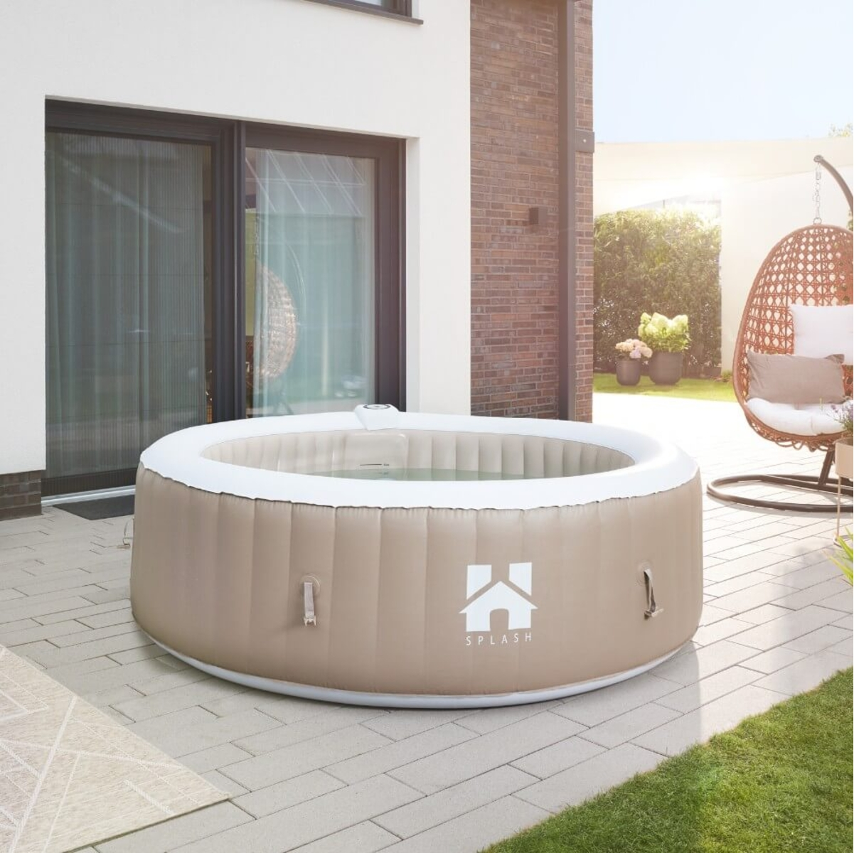 Ein Whirlpool im Freien steht auf einer Terrasse. Im Hintergrund befindet sich ein Haus mit einer Backsteinmauer. Rechts ist ein Hängestuhl.