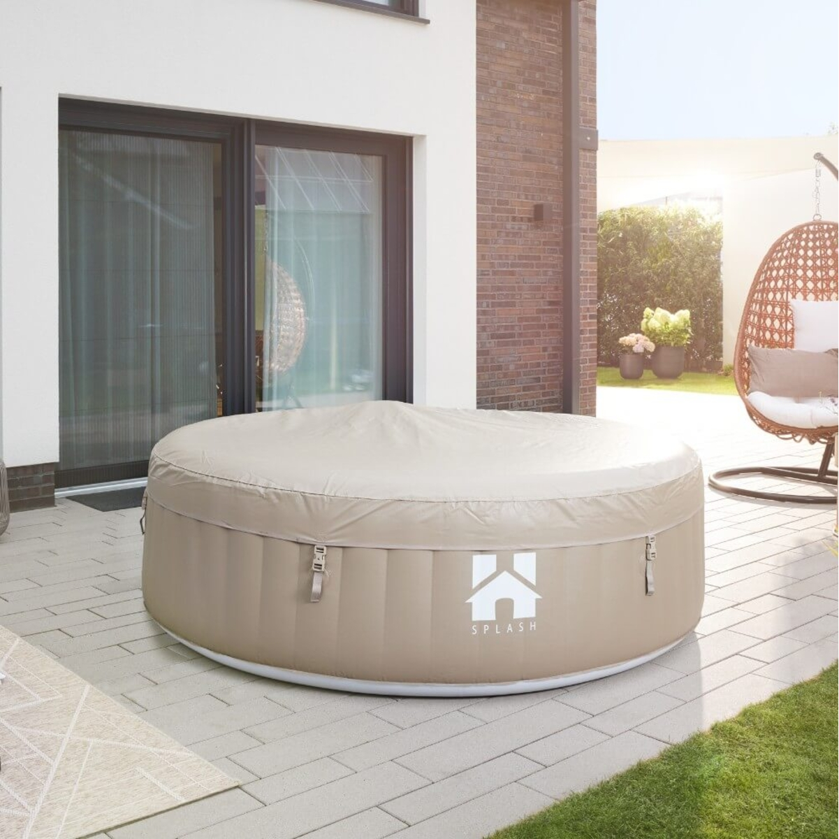Ein beigefarbenes, aufblasbares Whirlpool steht auf einer Terrasse. Eine Abdeckung ist darauf. Ein Haus und eine Terrasse mit Hängesessel sind im Hintergrund.