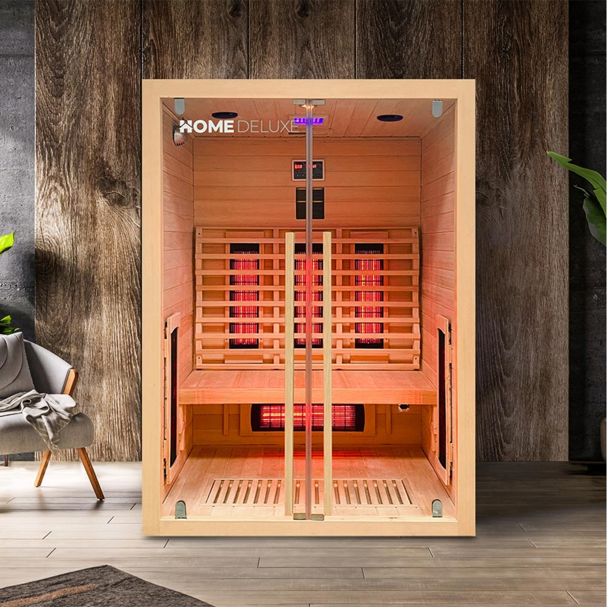 Holzsauna mit Glastür. Im Inneren sind rote Heizelemente sichtbar. Home Deluxe Logo oben. Links ein Stuhl.