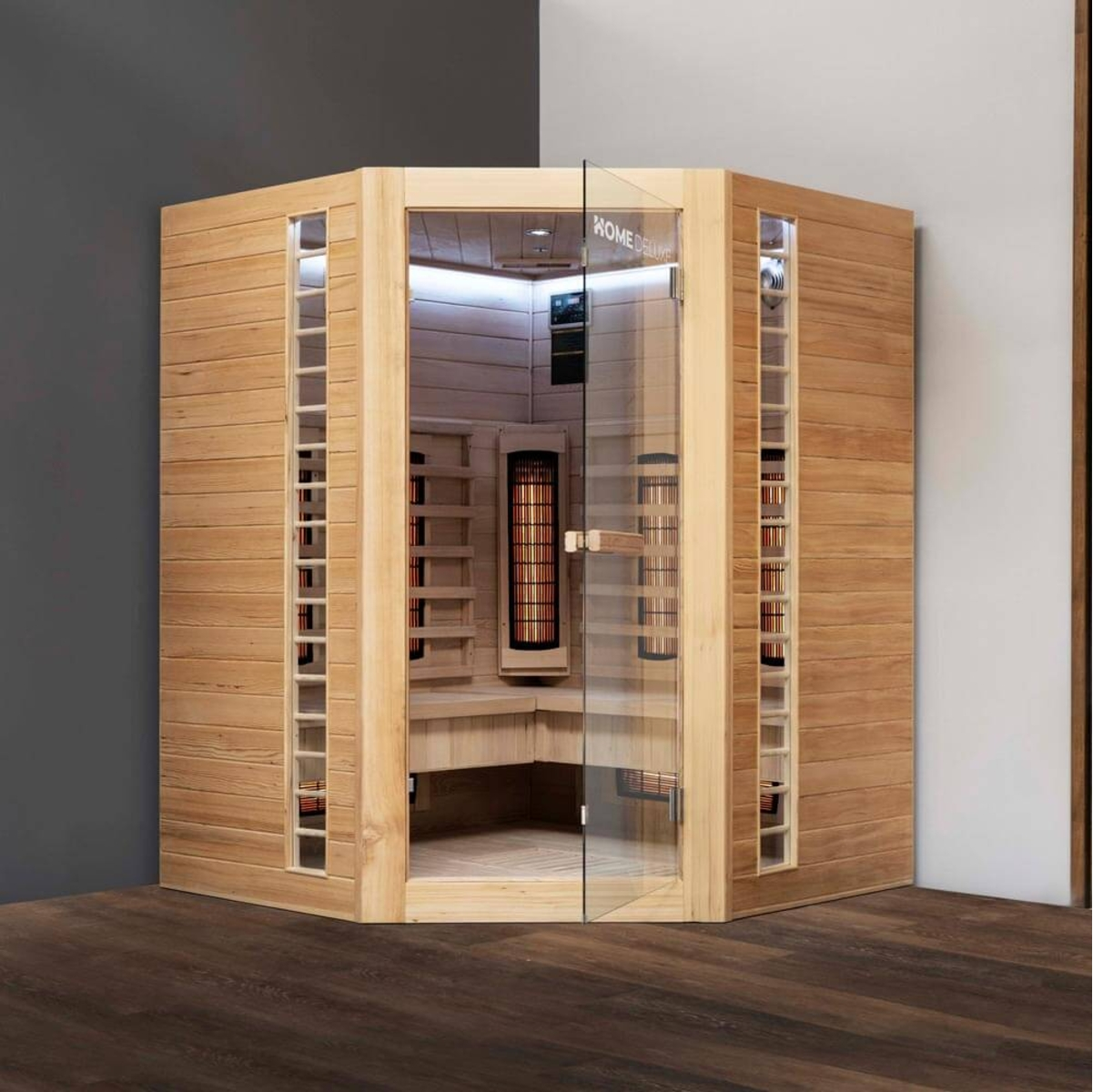 Eine Holzsauna mit Glastür. Im Inneren befinden sich ein Heizgerät und Bänke. Die Sauna ist beleuchtet und steht auf einem dunklen Holzboden.