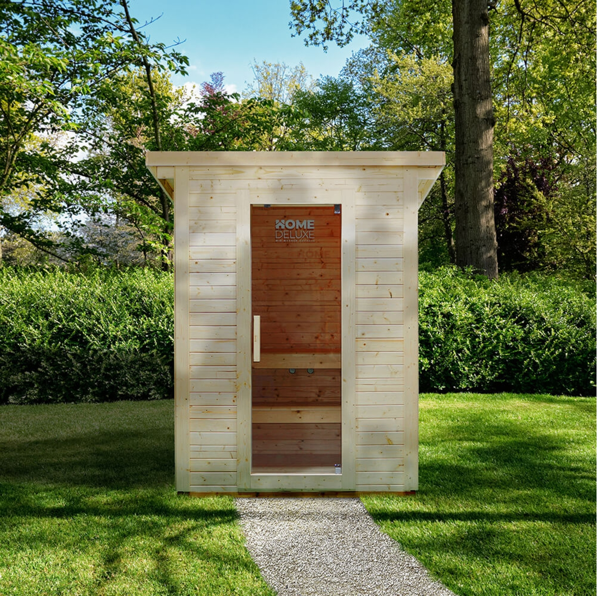 Eine Holzsauna mit Glastür steht auf einem Kiesweg in einem grünen Garten. Bäume und Büsche umgeben sie, und der Himmel ist blau.