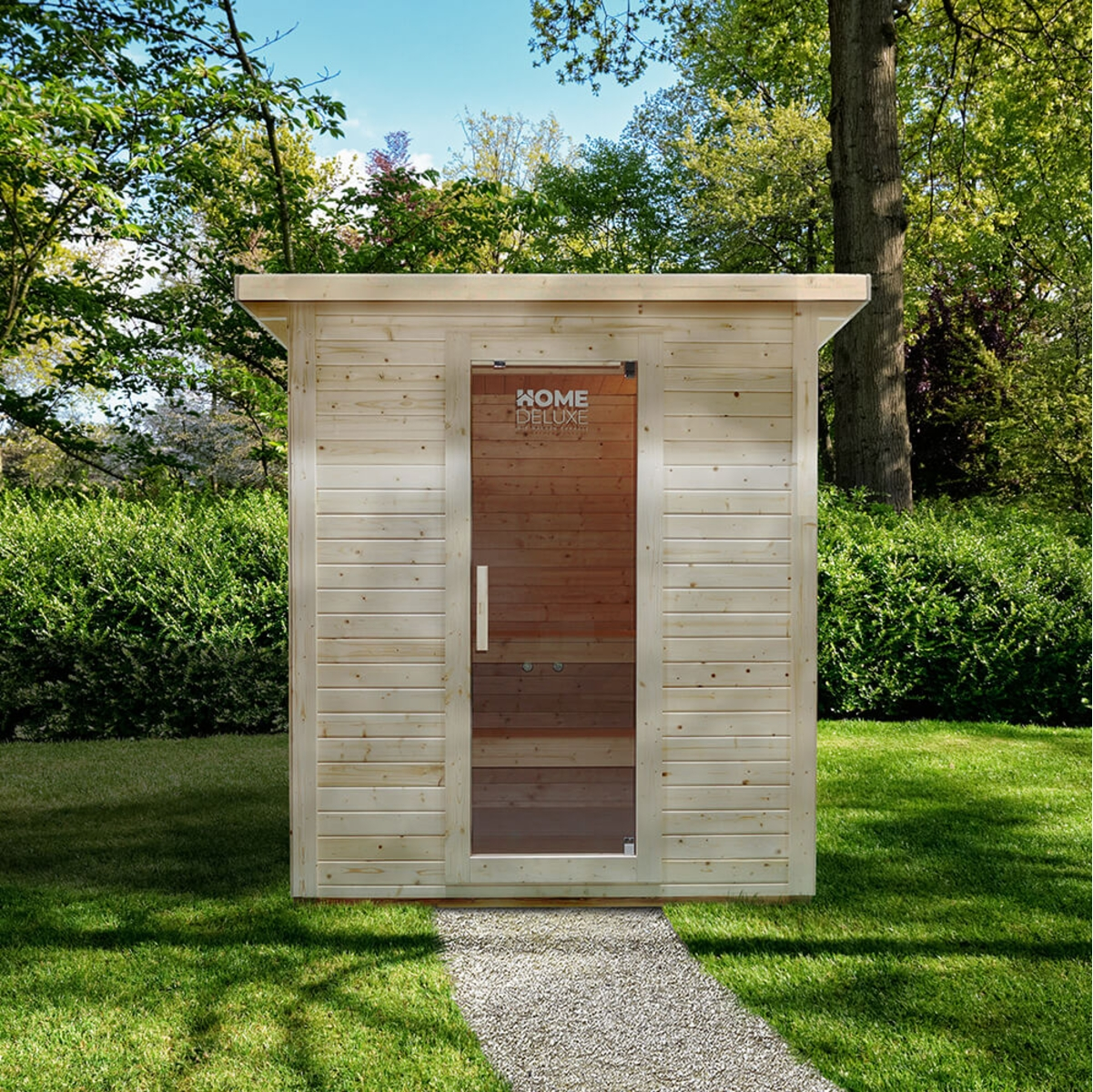Eine Holzsauna mit Glastür steht in einem grasbewachsenen Hof. Ein Steinweg führt zur Sauna. Bäume und Büsche umgeben sie unter blauem Himmel.