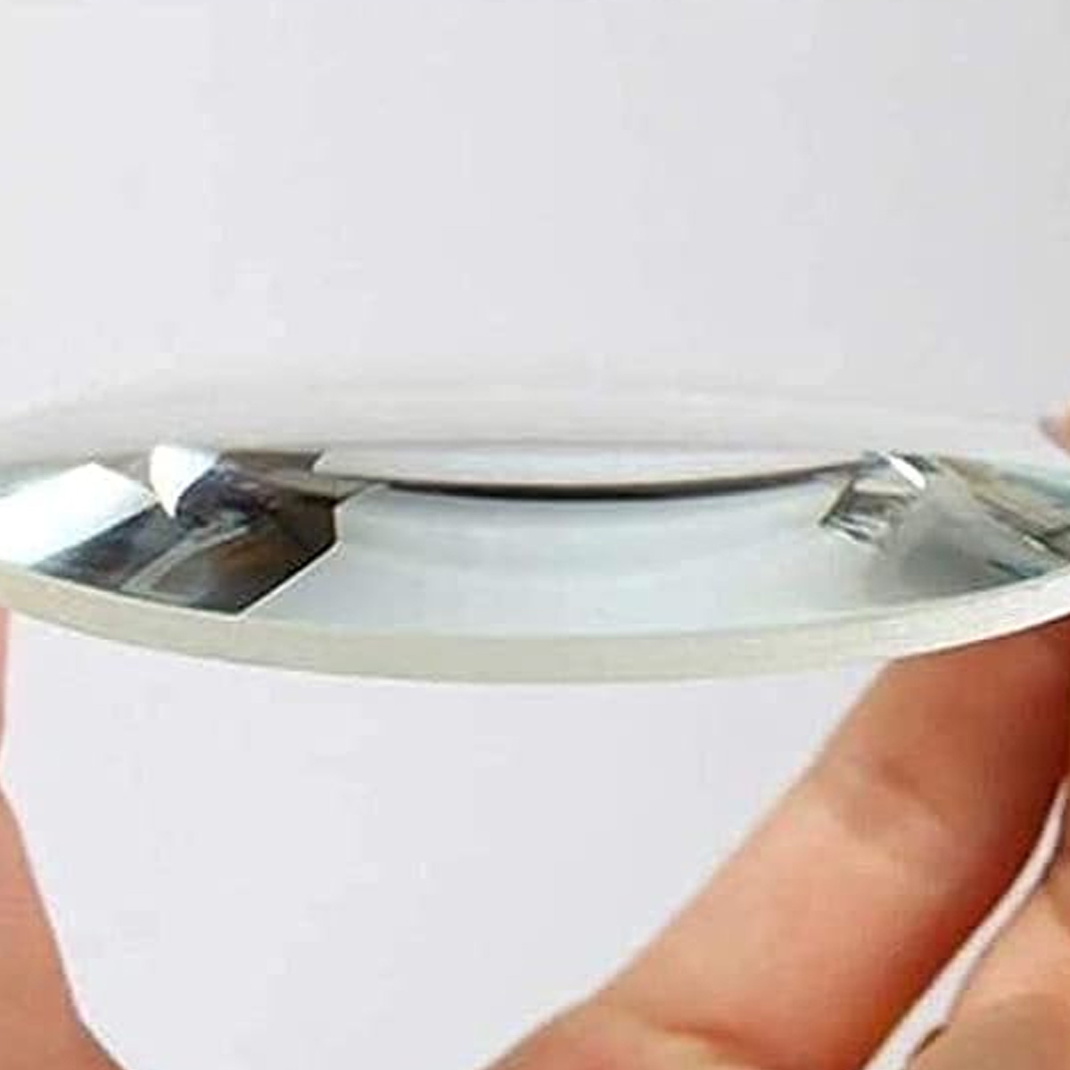 Eine klare Lupe wird zwischen zwei Händen gehalten. Das Glas hat eine leicht gekrümmte Oberfläche. Der Hintergrund ist weiß.