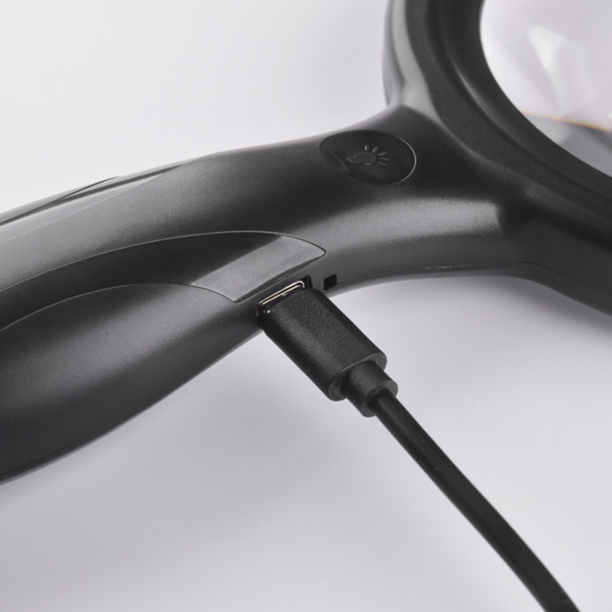 Eine schwarze Lupe mit eingestecktem Ladekabel. Der Hintergrund ist weiß.