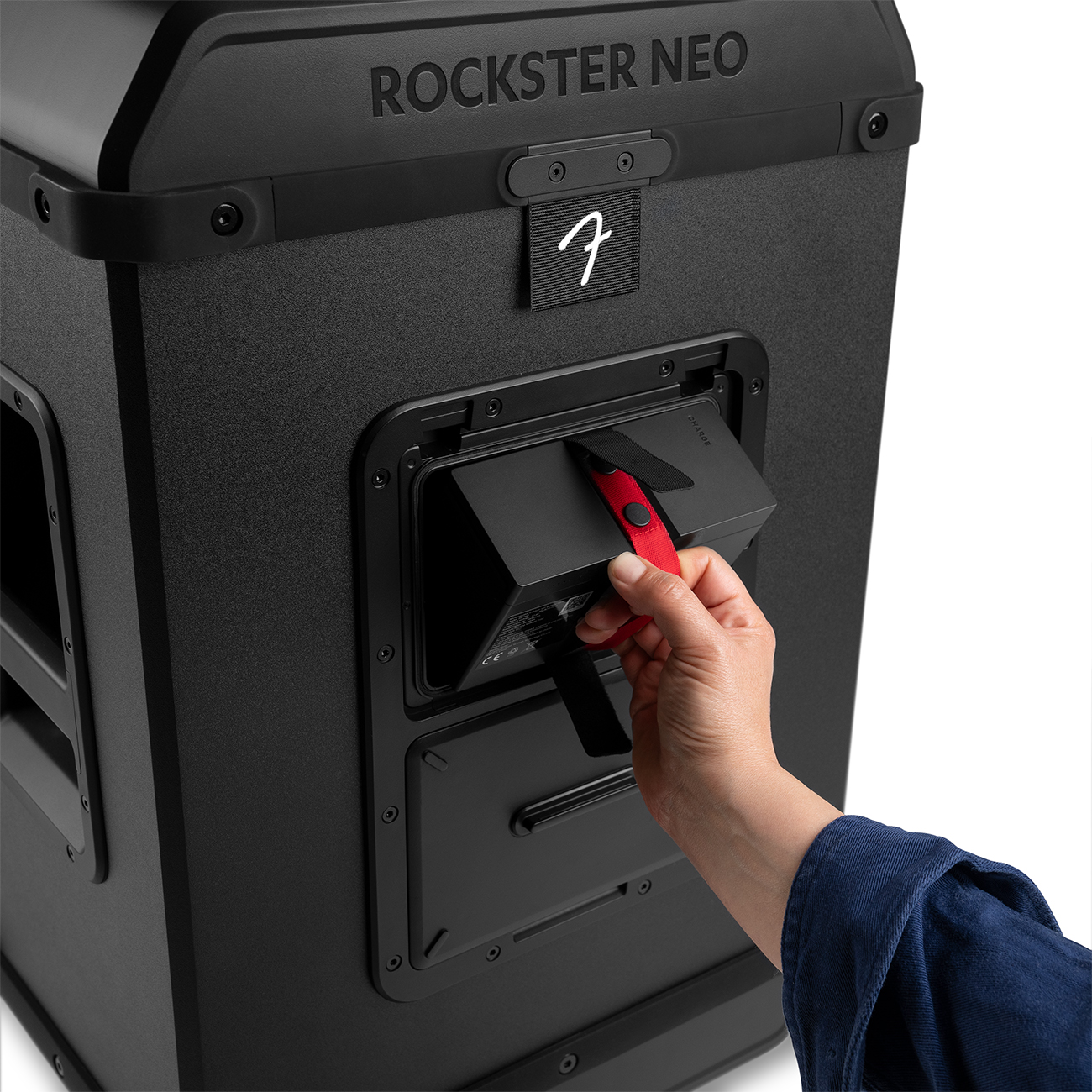 Een hand trekt aan een rode riem op een zwarte Rockster Neo-luidspreker. De luidspreker heeft een Fender-logo en 'ROCKSTER NEO' bovenaan.