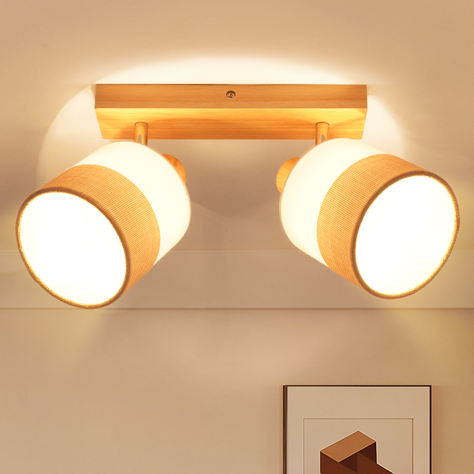 Lampa sufitowa. Dwie lampy z materiałowymi kloszami, zamontowane na drewnianej podstawie. Jasnobeżowa ściana, poniżej grafika.