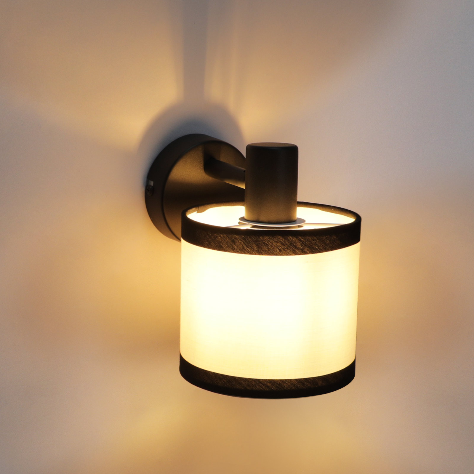 Una lampada da parete con paralume cilindrico. La lampada è nera ed emette una luce calda e invitante.