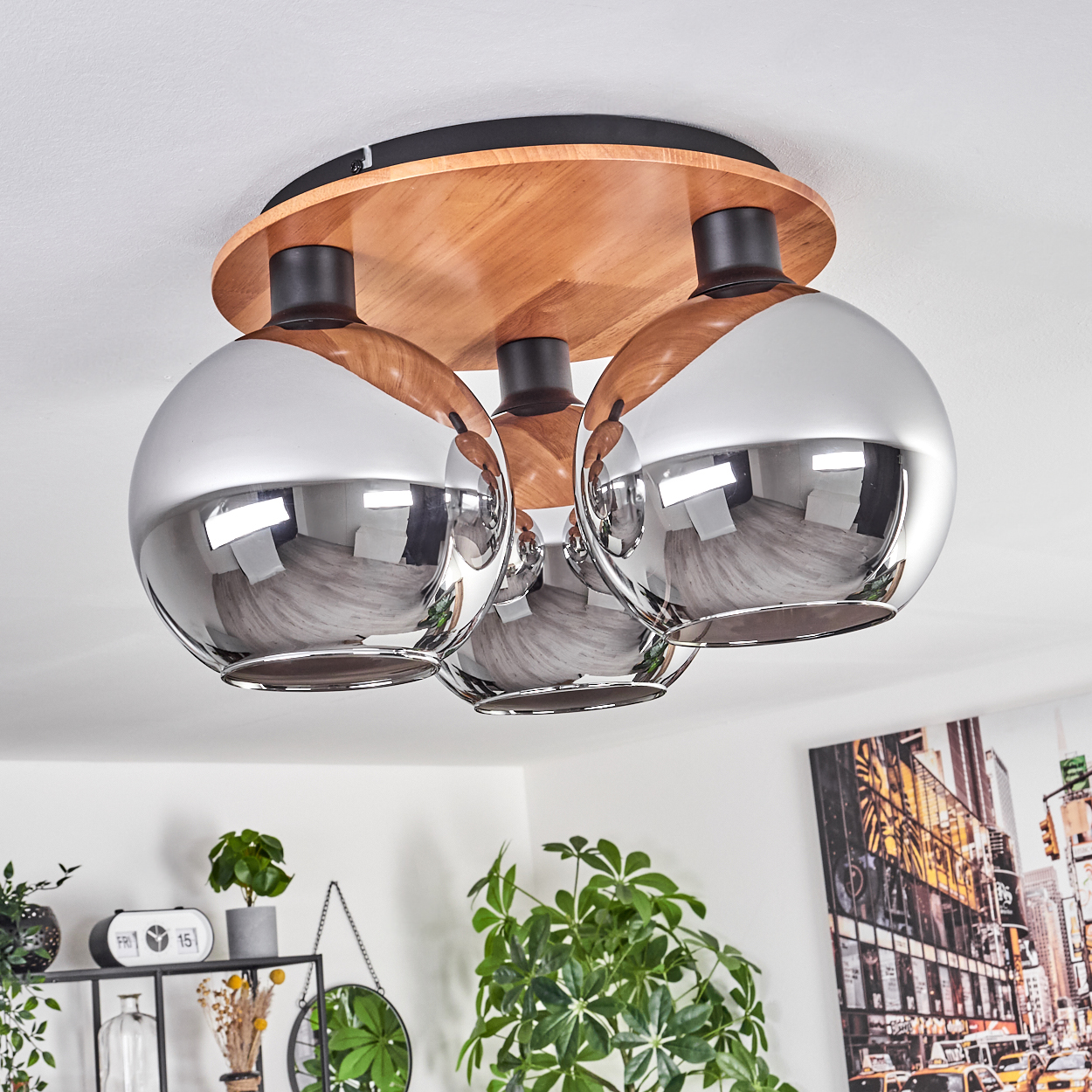 Eine Deckenlampe mit drei verchromten Kugelleuchten. Holzsockel und schwarze Akzente, mit Pflanzen und Stadtkunst im Hintergrund.