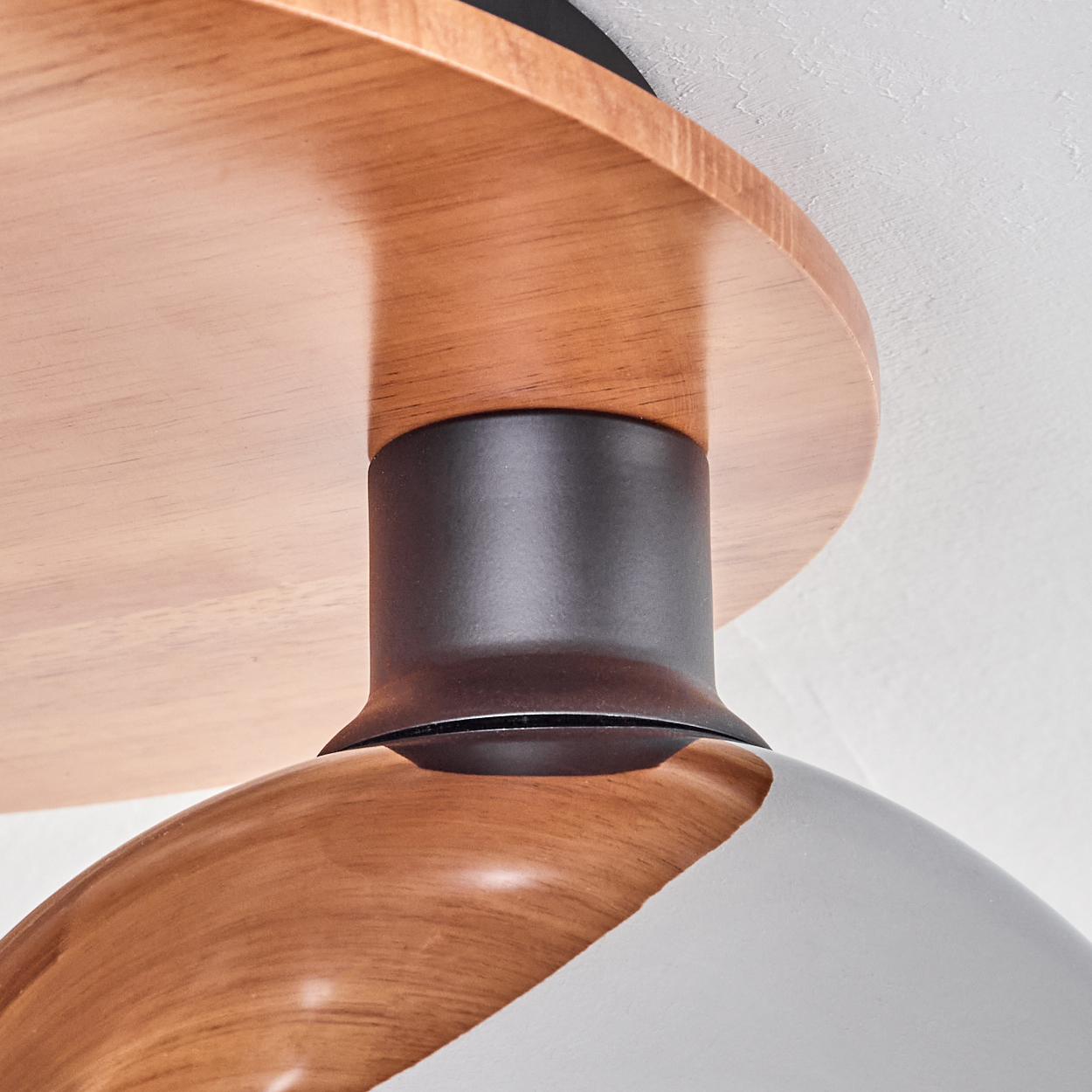 Nahaufnahme einer Holzleuchte. Sie hat einen braunen Holzschirm, einen schwarzen Metallschaft und einen grau-braunen gebogenen Boden.
