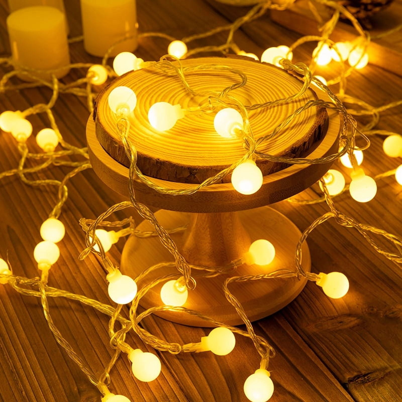 Eine warme, gemütliche Szene mit leuchtenden Lichterketten. Ein Holzständer hält Lichter, und zwei Kerzen sind im Hintergrund.