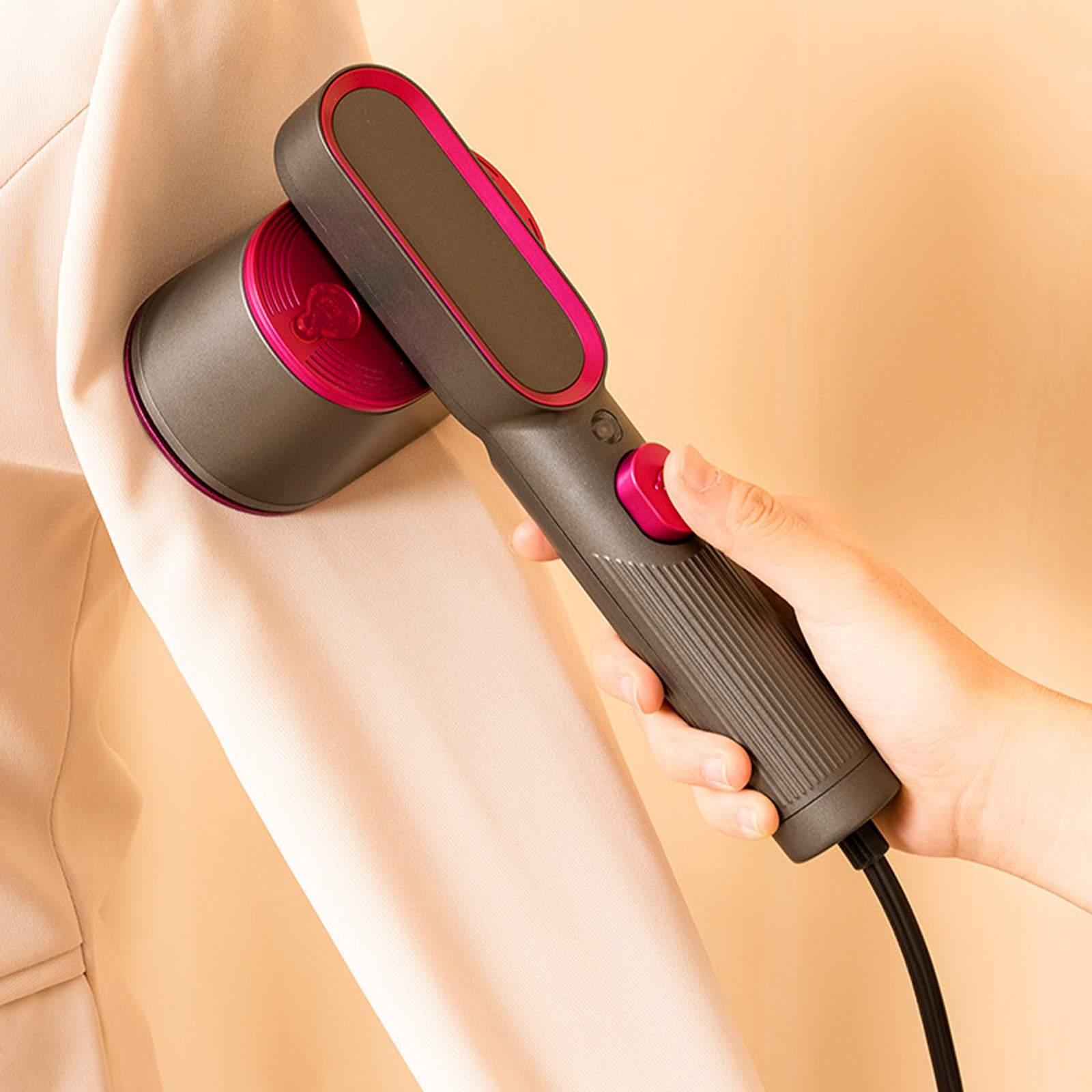 Eine Person benutzt einen Handdampfer auf einer hellen Jacke. Der Dampfer ist grau und rosa. Der Hintergrund ist cremefarben.
