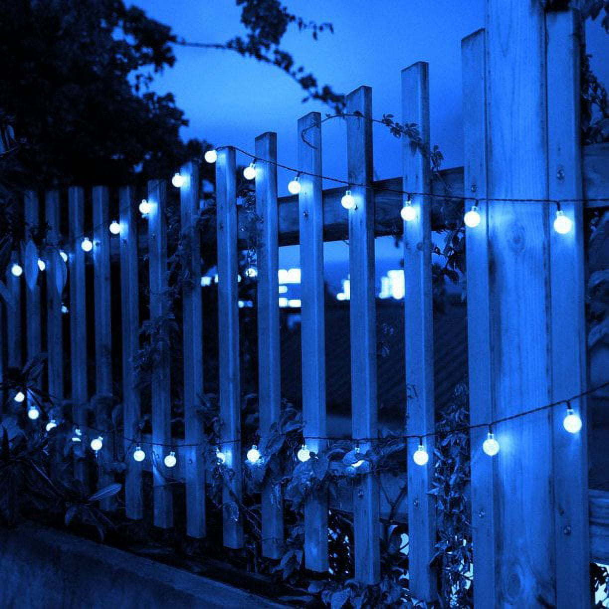 Holzzaun mit Lichterketten. Blauer Farbton. Laub. Abendszene.