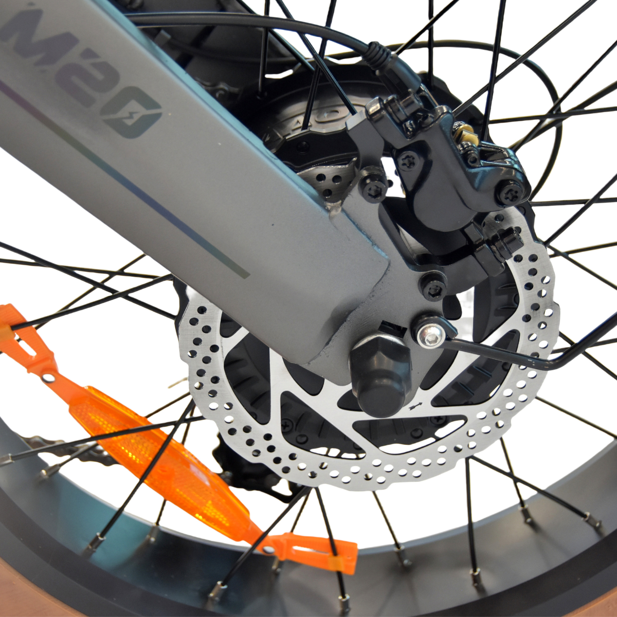 Zbliżenie koła roweru z hamulcem tarczowym, czarnymi szprychami i pomarańczowym odblaskiem.