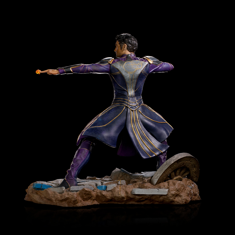 Una figura in abito viola e oro, con un globo luminoso, su una base rocciosa. Sfondo nero.