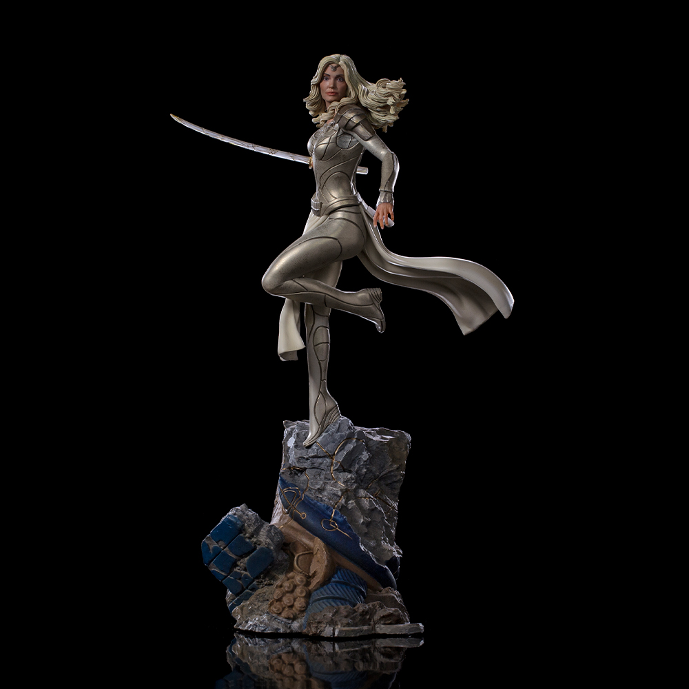 Statua di donna in armatura d'argento con spada, su base rocciosa, sfondo nero.