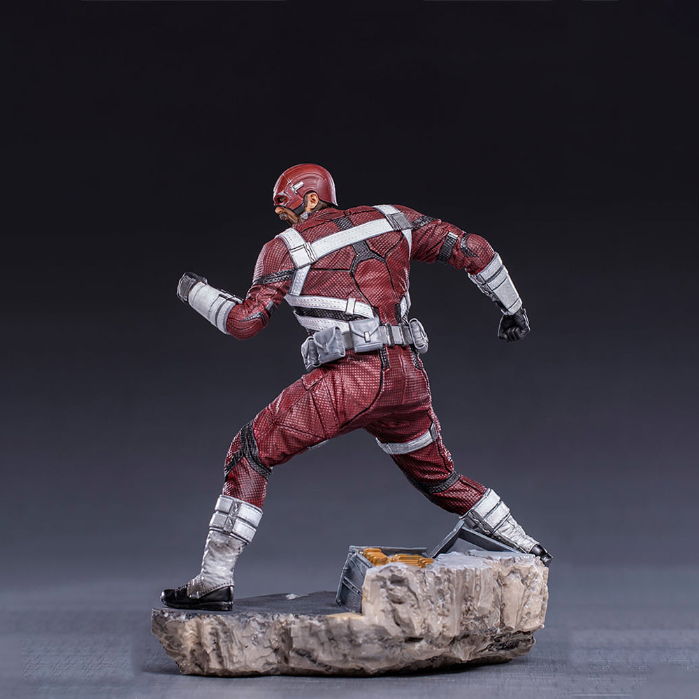 Una statuetta di un uomo in tuta rossa e bianca che corre. È su una base rocciosa. Lo sfondo è scuro.