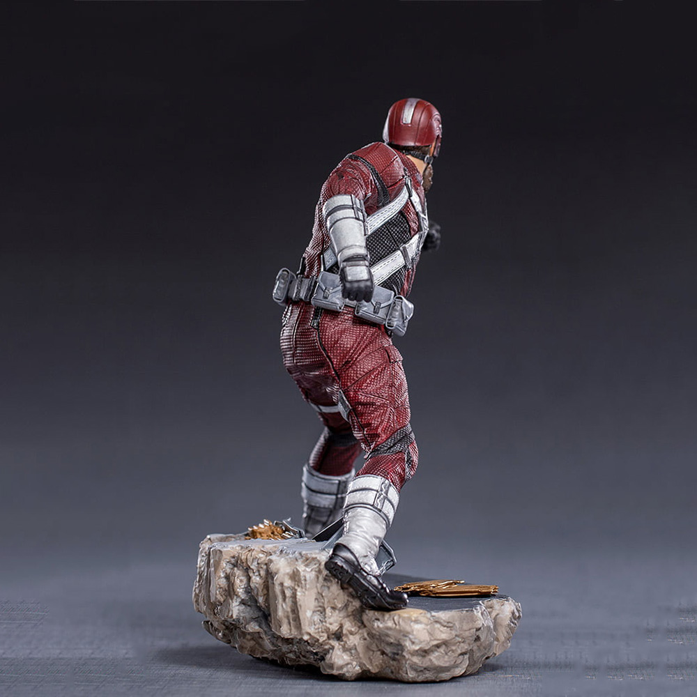 Una statuetta di Red Guardian in tuta rossa e bianca, casco e stivali neri, in piedi su una base rocciosa, con sfondo scuro.