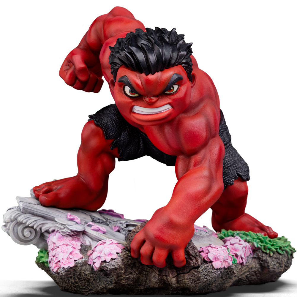 Una statuina rossa di Hulk si accovaccia, pronta. Capelli neri, volto arrabbiato. Si trova su una base di roccia con fiori rosa ed erba verde.