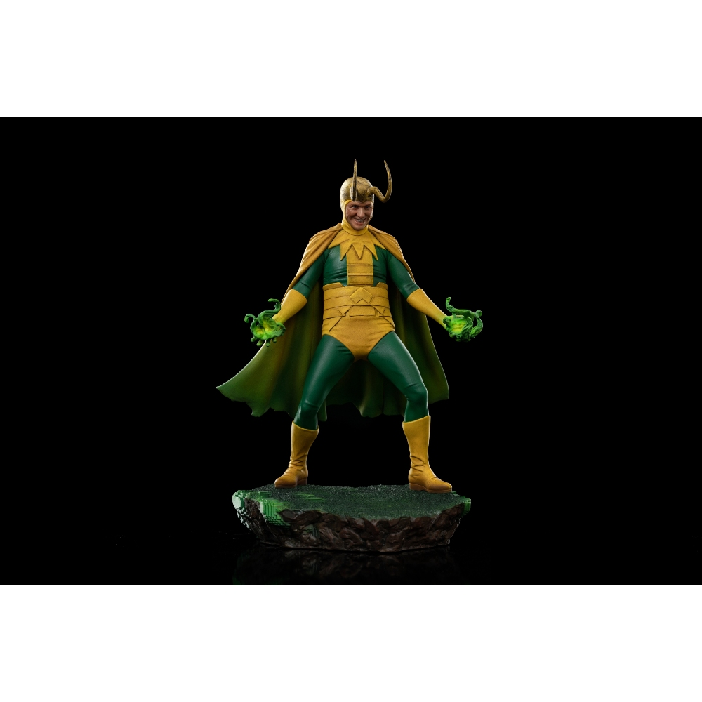 Una statuetta di Loki con costume verde e giallo e mantello. Tiene globi verdi luminosi. Sfondo scuro.