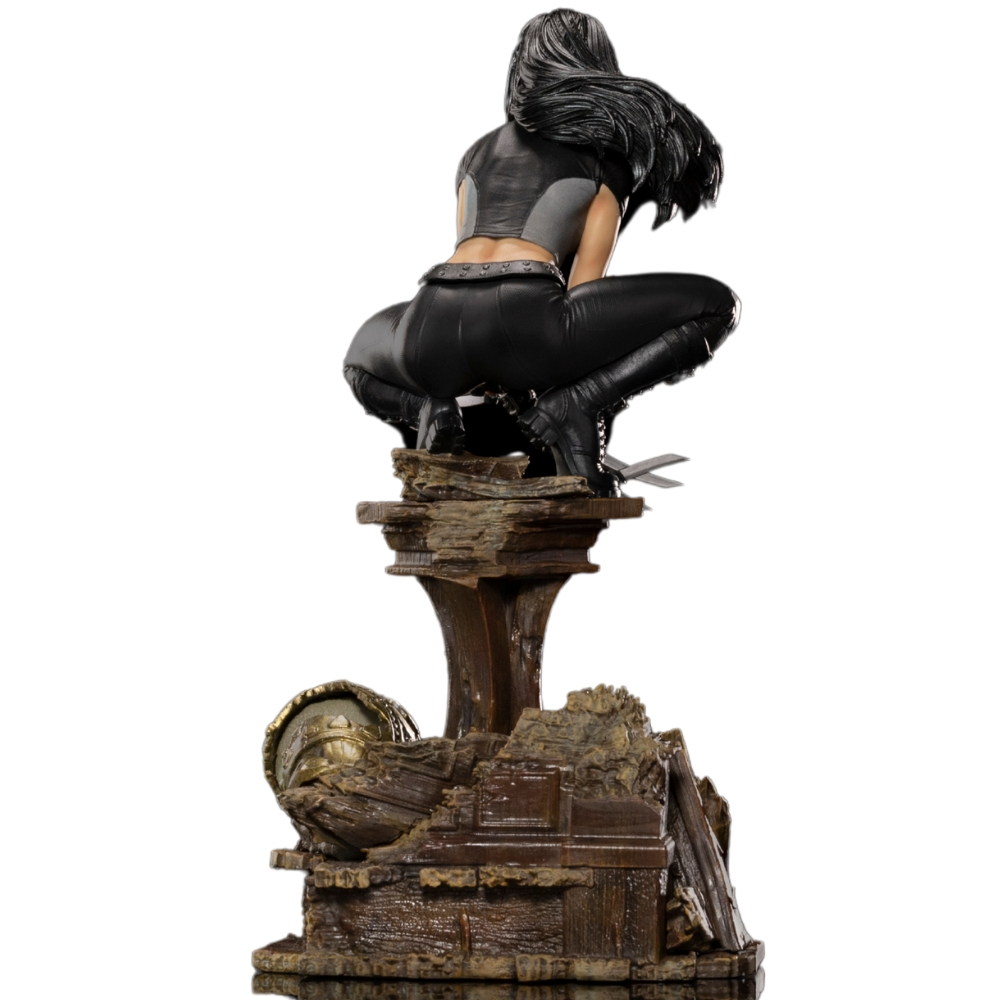 Statua di donna in pelle nera accovacciata su piedistallo di pietra. Un elmo alla base. Lame visibili.