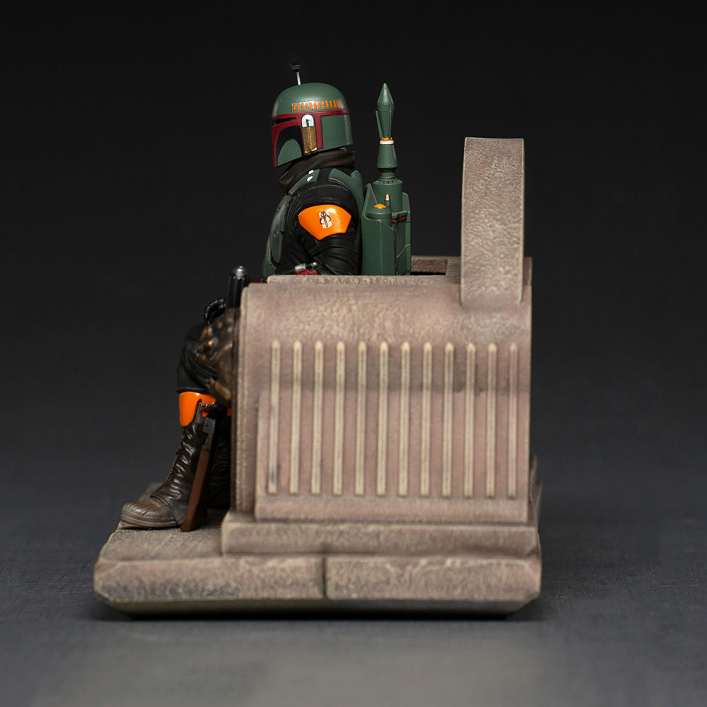 Figura di Boba Fett seduta su un trono. Indossa un'armatura verde e arancione e un casco. Il trono è marrone con linee verticali.