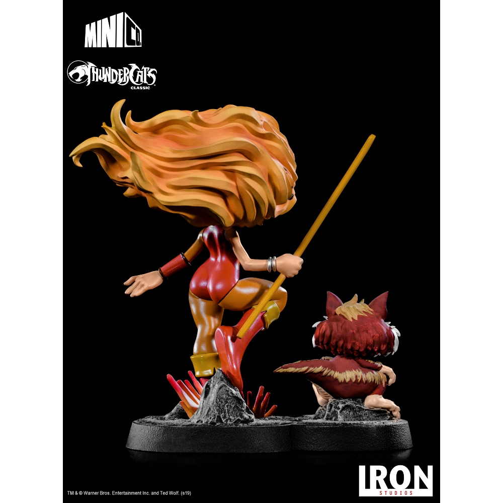 Una statua di un personaggio dei Thundercats con un bastone e una figura più piccola. Lo sfondo è nero. La statua è su una base.