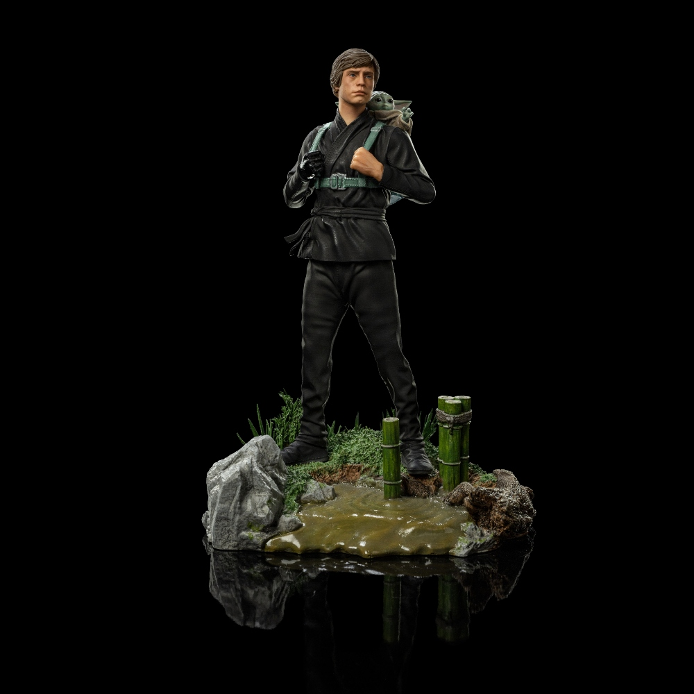 Eine Figur von Luke Skywalker in schwarzer Kleidung mit Grogu auf der Schulter, stehend auf einem kleinen Diorama mit Wasser und Bambus.