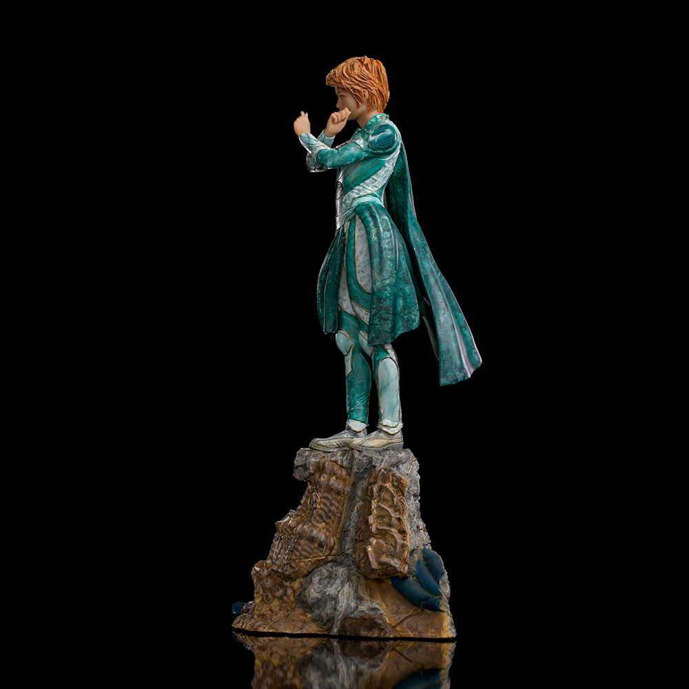 Statua di una persona con armatura verde acqua in piedi su una roccia contro uno sfondo nero. Stanno alzando le mani.