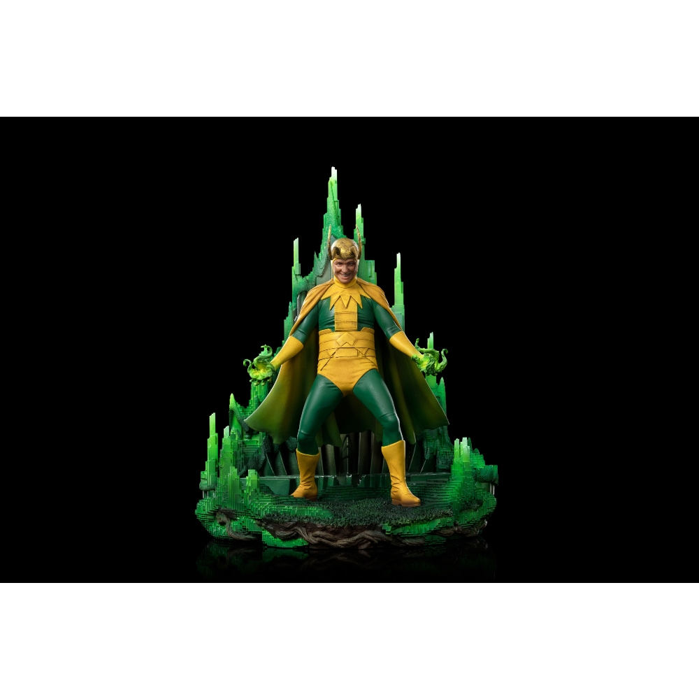 Una statuetta di Loki in costume verde e giallo, in piedi davanti a una struttura di cristallo verde. Sfondo nero.