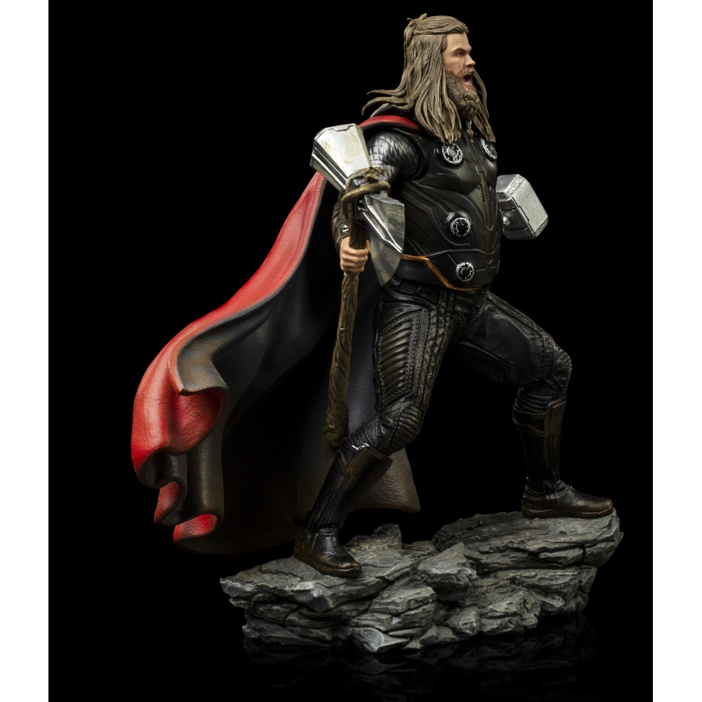 Una statua di Thor. Tiene un martello e indossa un'armatura nera con un mantello rosso. È in piedi su una roccia su uno sfondo nero.